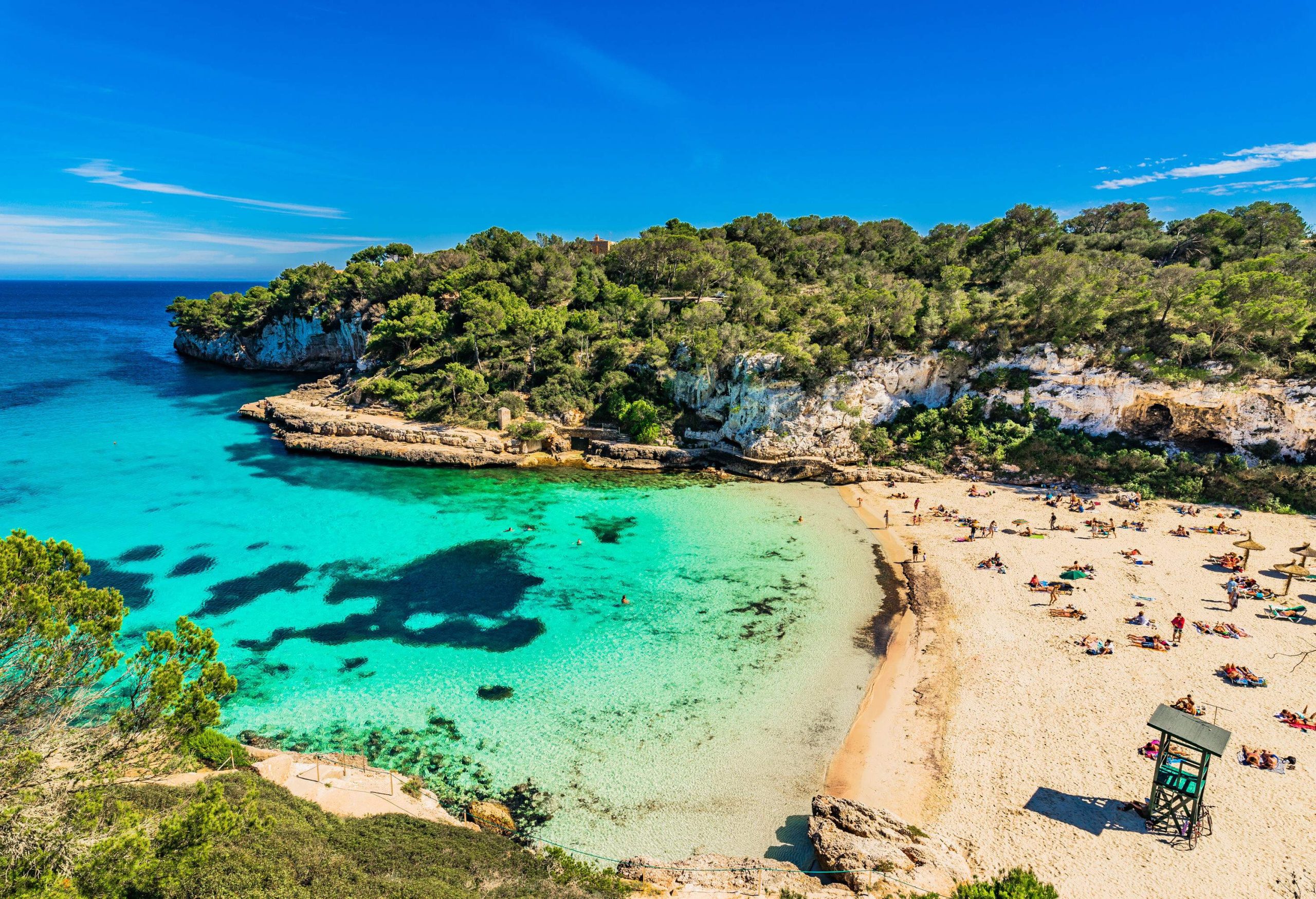 A bay with stunning blue seas and people basking in the sun on the sand.