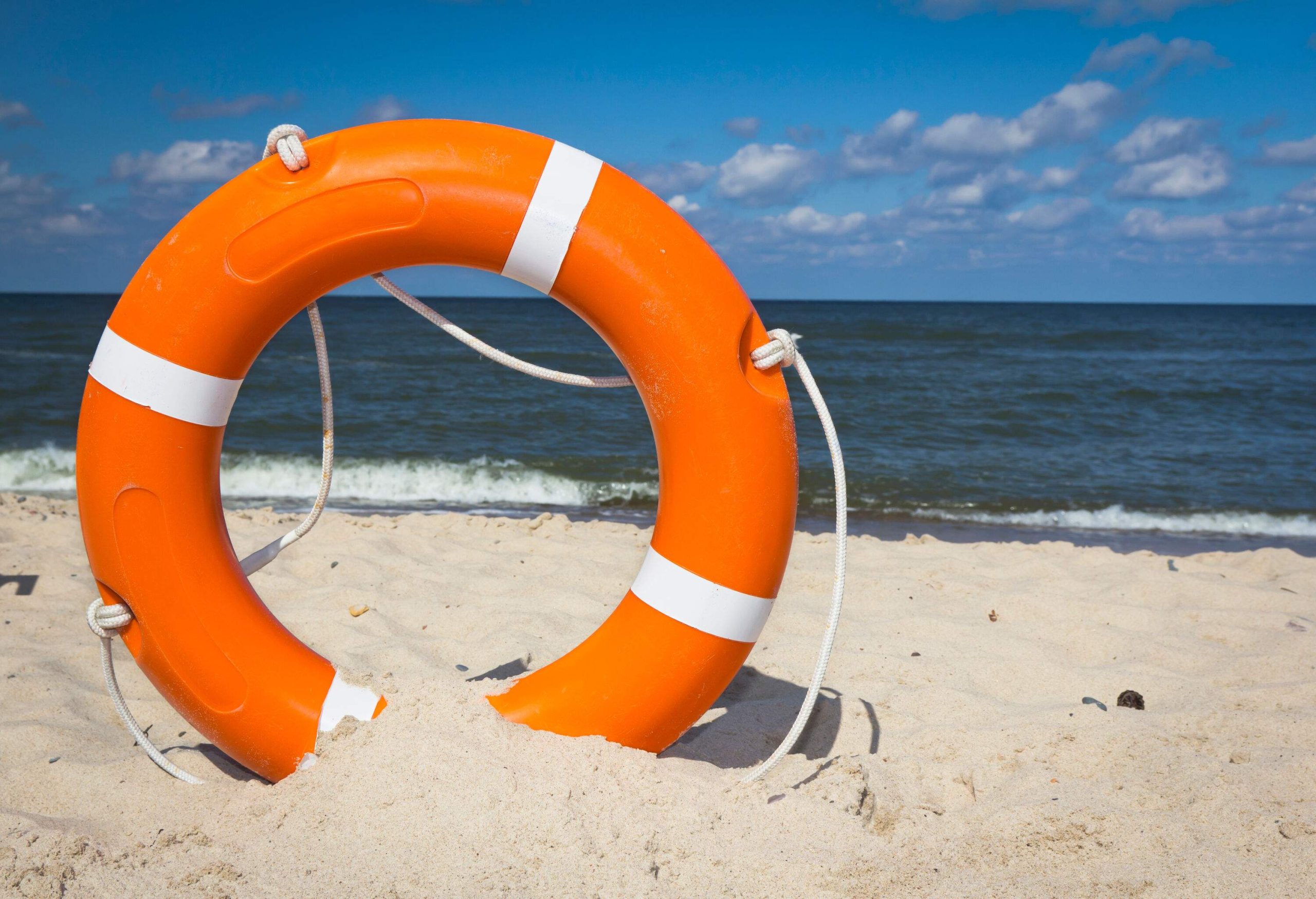 An orange lifebuoy ring with a rope stands along the beach's fine white sand.