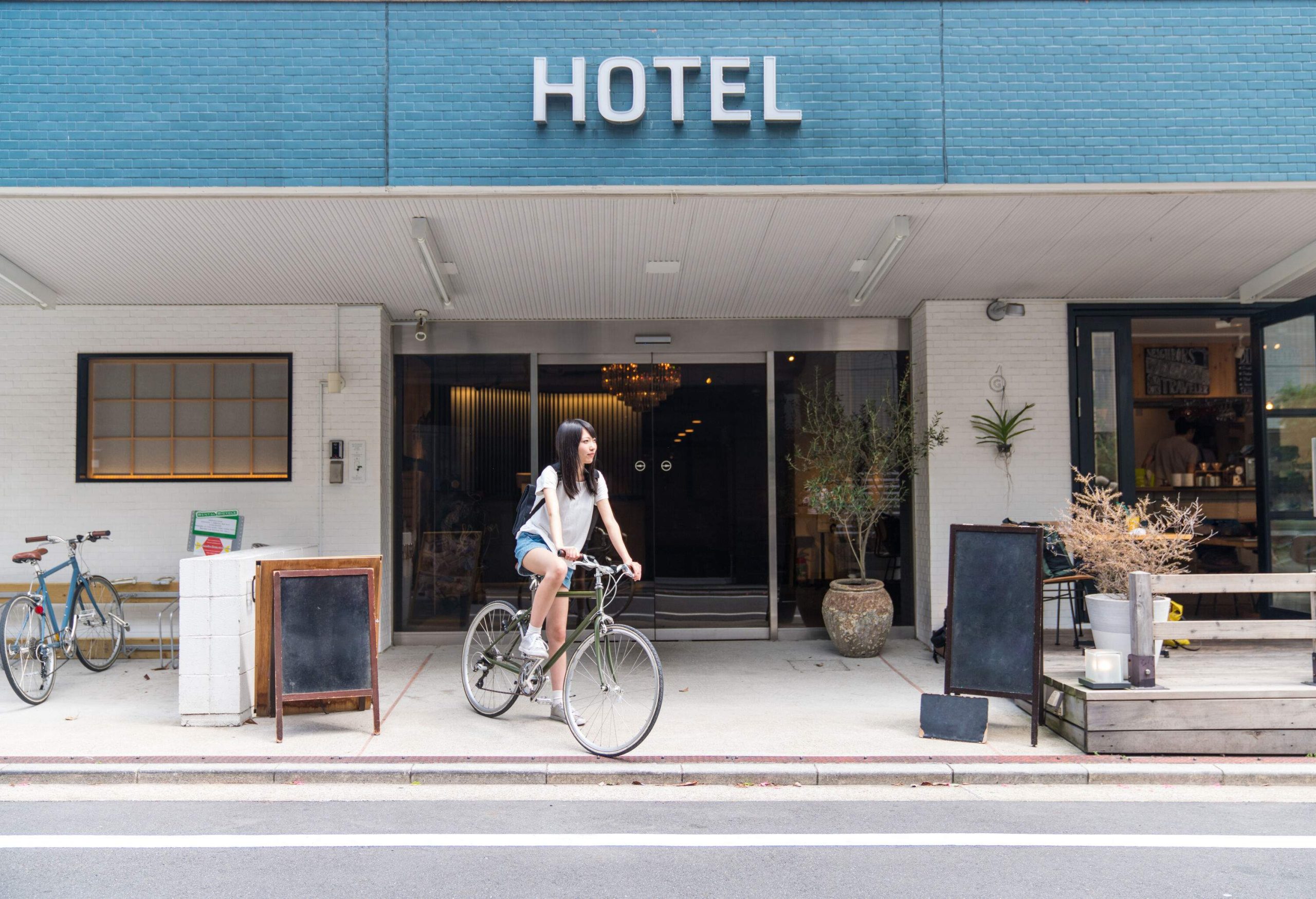 A girl rides on a bicycle at the entrance of a hotel.