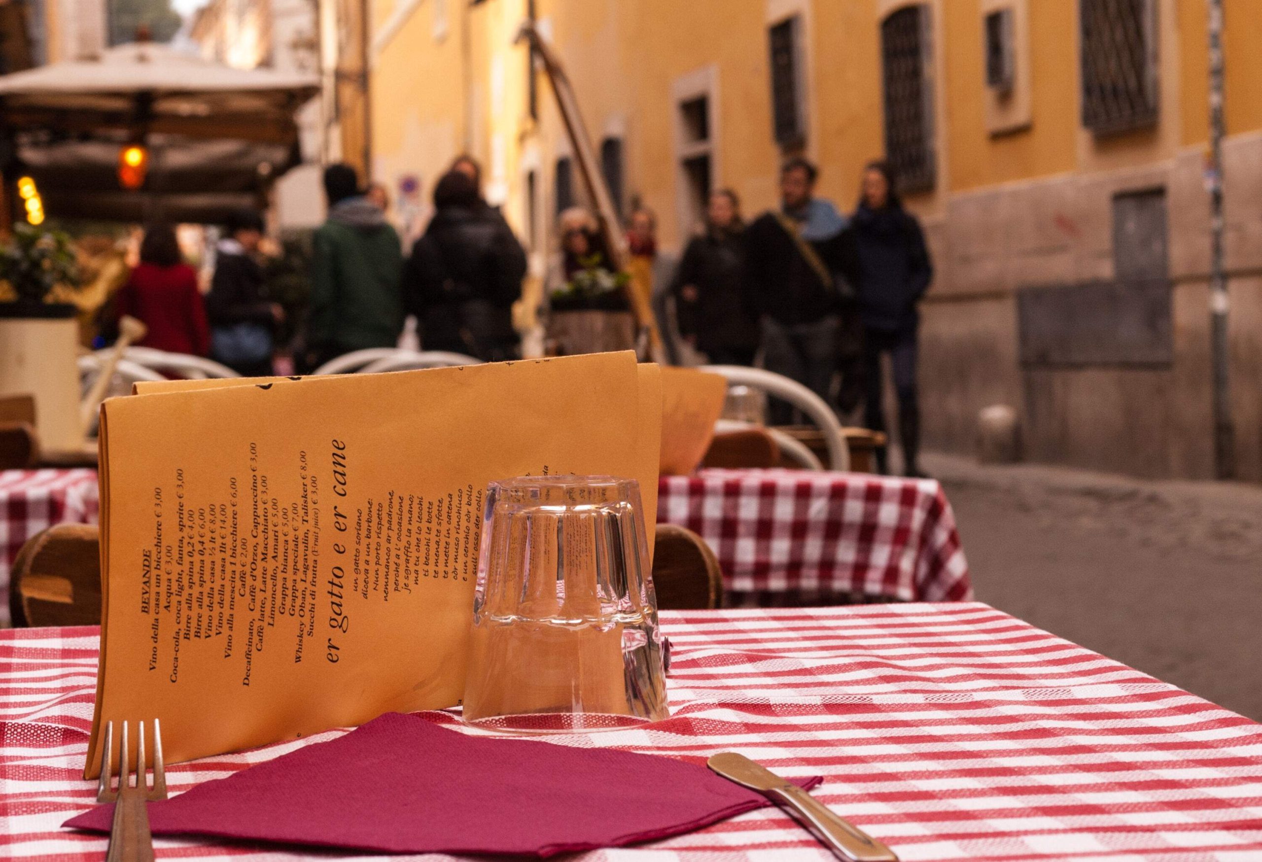 A table covered with a red-white cloth arranged with a fork, a knife, an inverted glass, a paper napkin, and a menu.