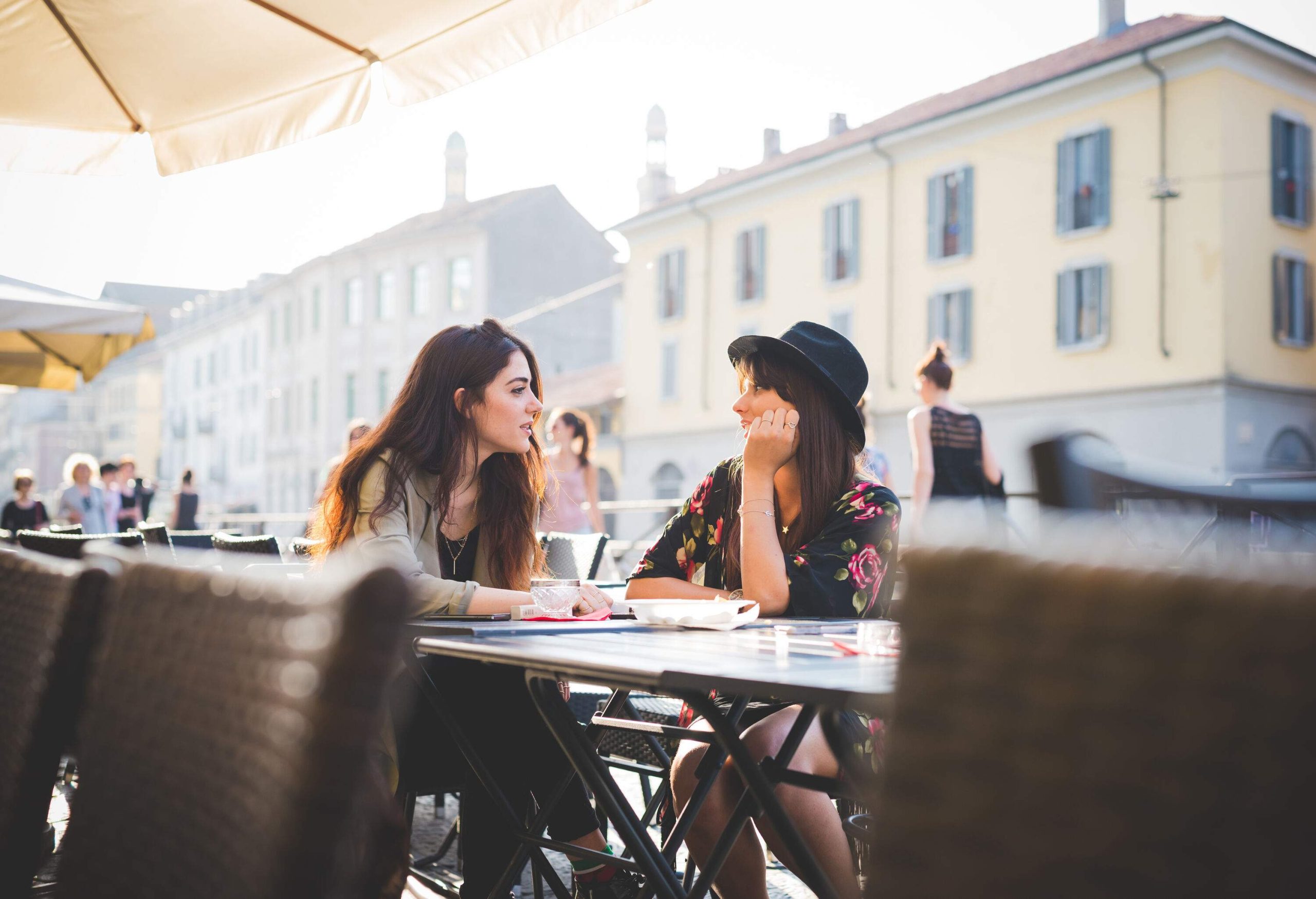 Two female friends tell stories while dining in a restaurant outdoors.