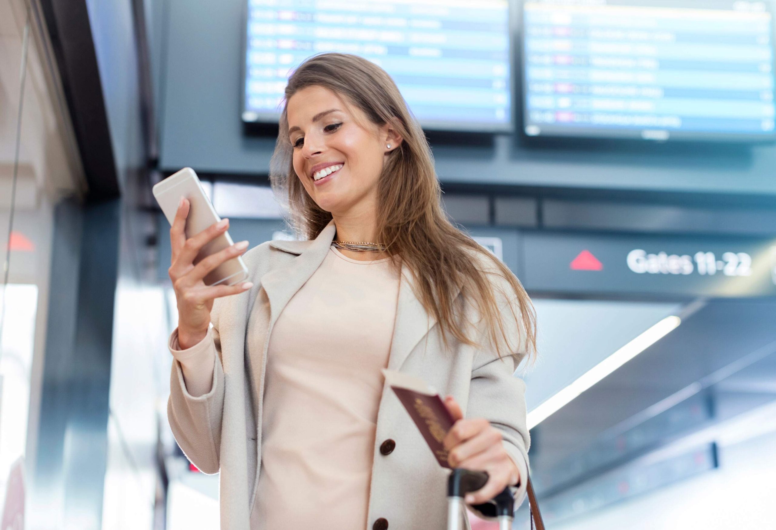 A woman holding a passport while using her phone in an airport.