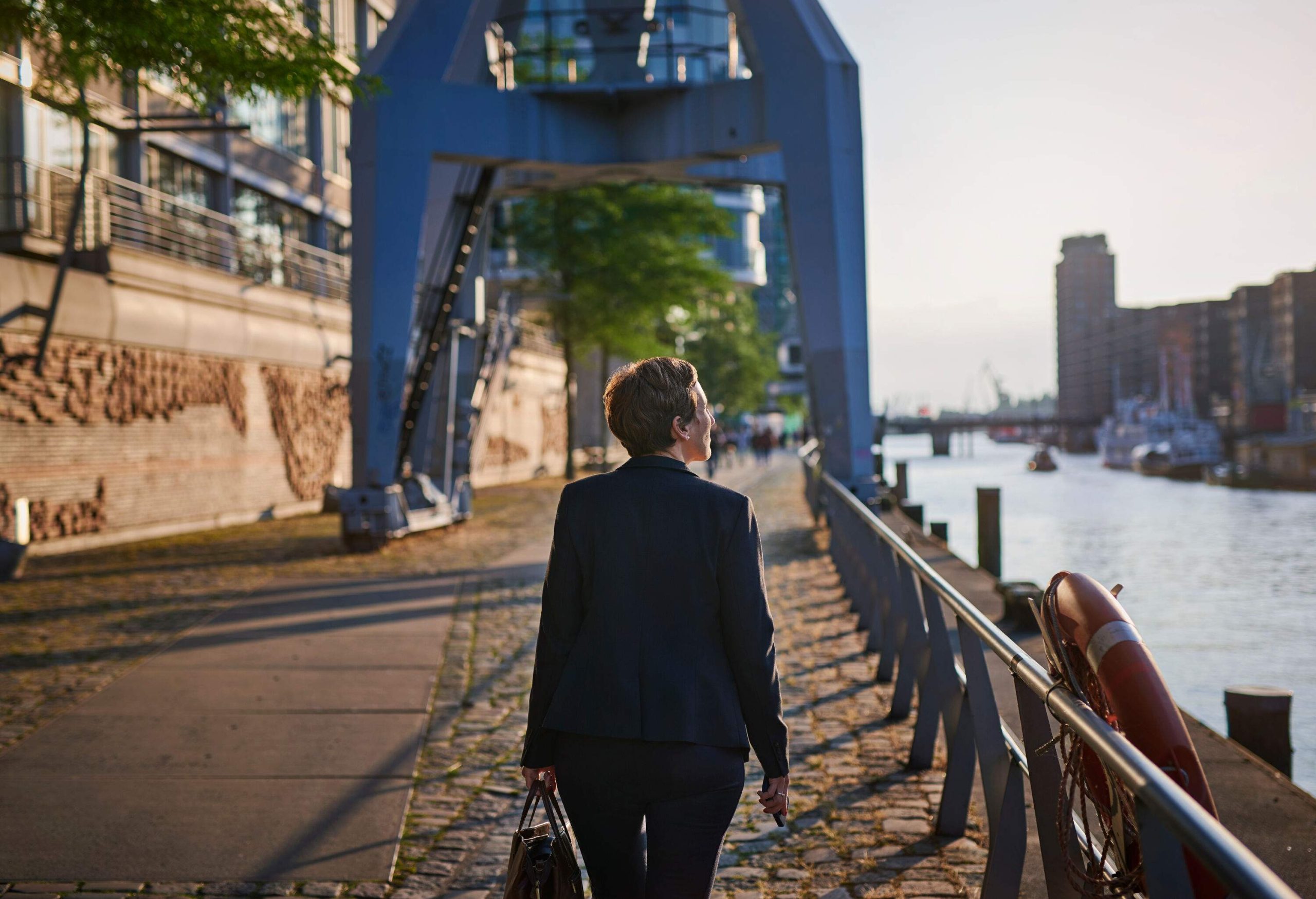 Next to the river's railing, a businesswoman walks while enjoying the sunset light.