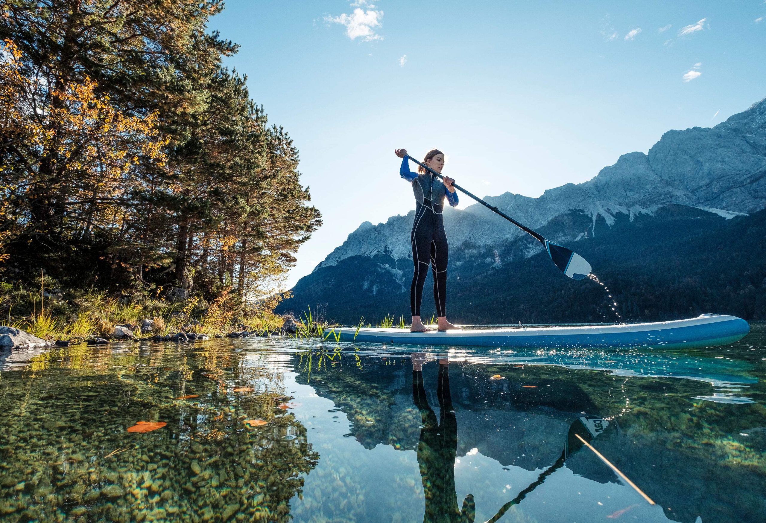 A woman standup paddleboarding in a crystal clear lake beneath the mountains.