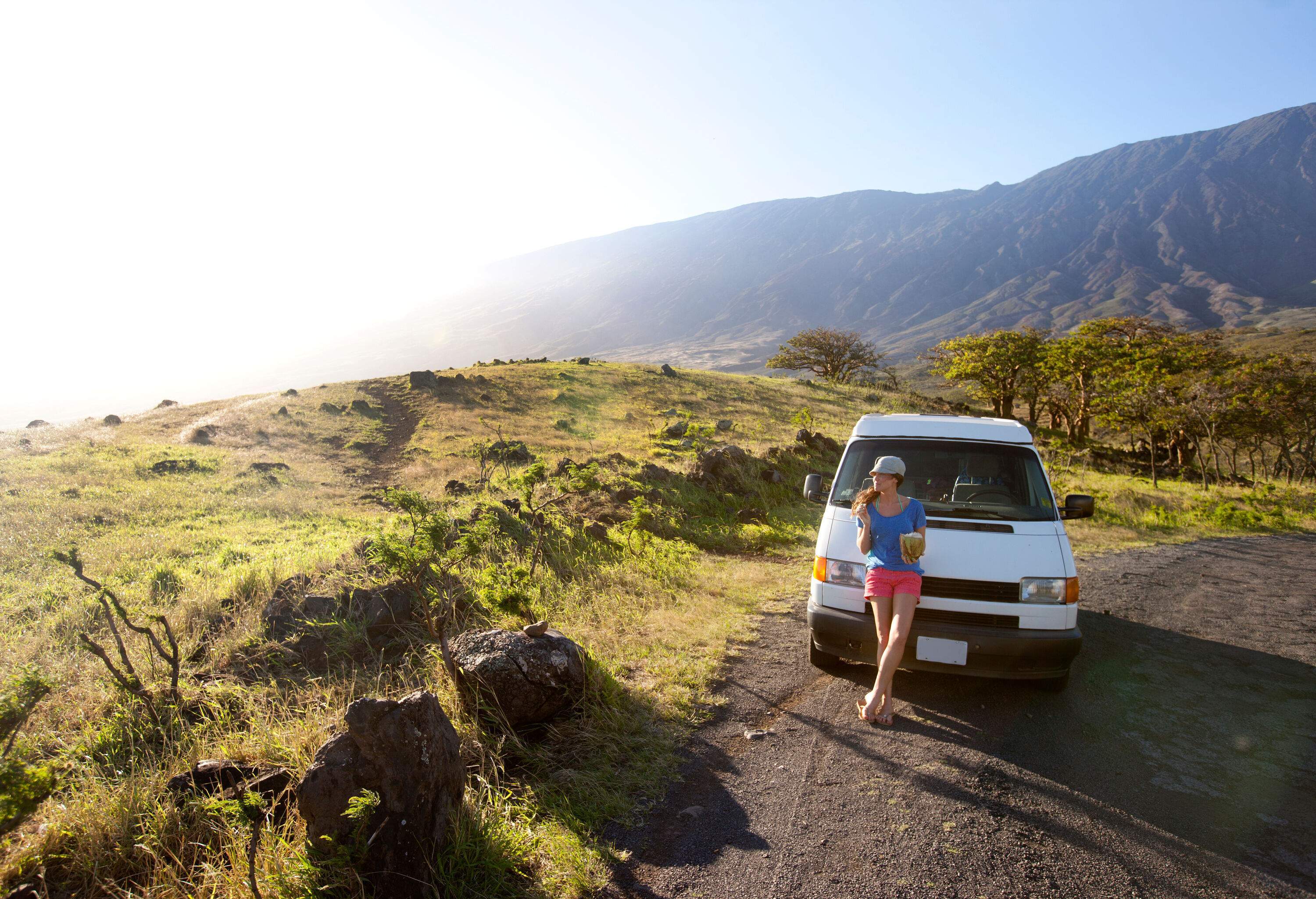 A woman stops to drink a fresh coconut while driving the road to Hana.