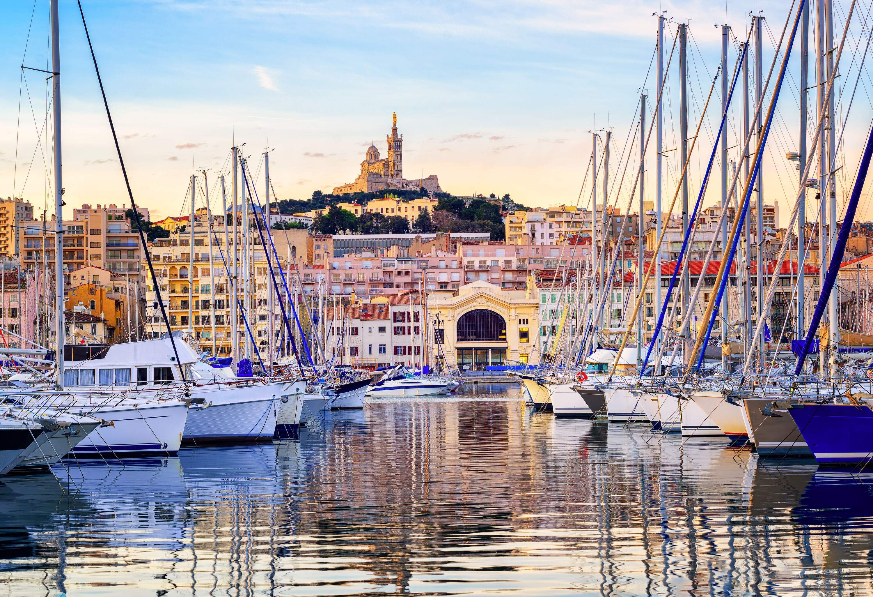 A harbour with docked boats with views of waterfront buildings and a hilltop church with a tower.