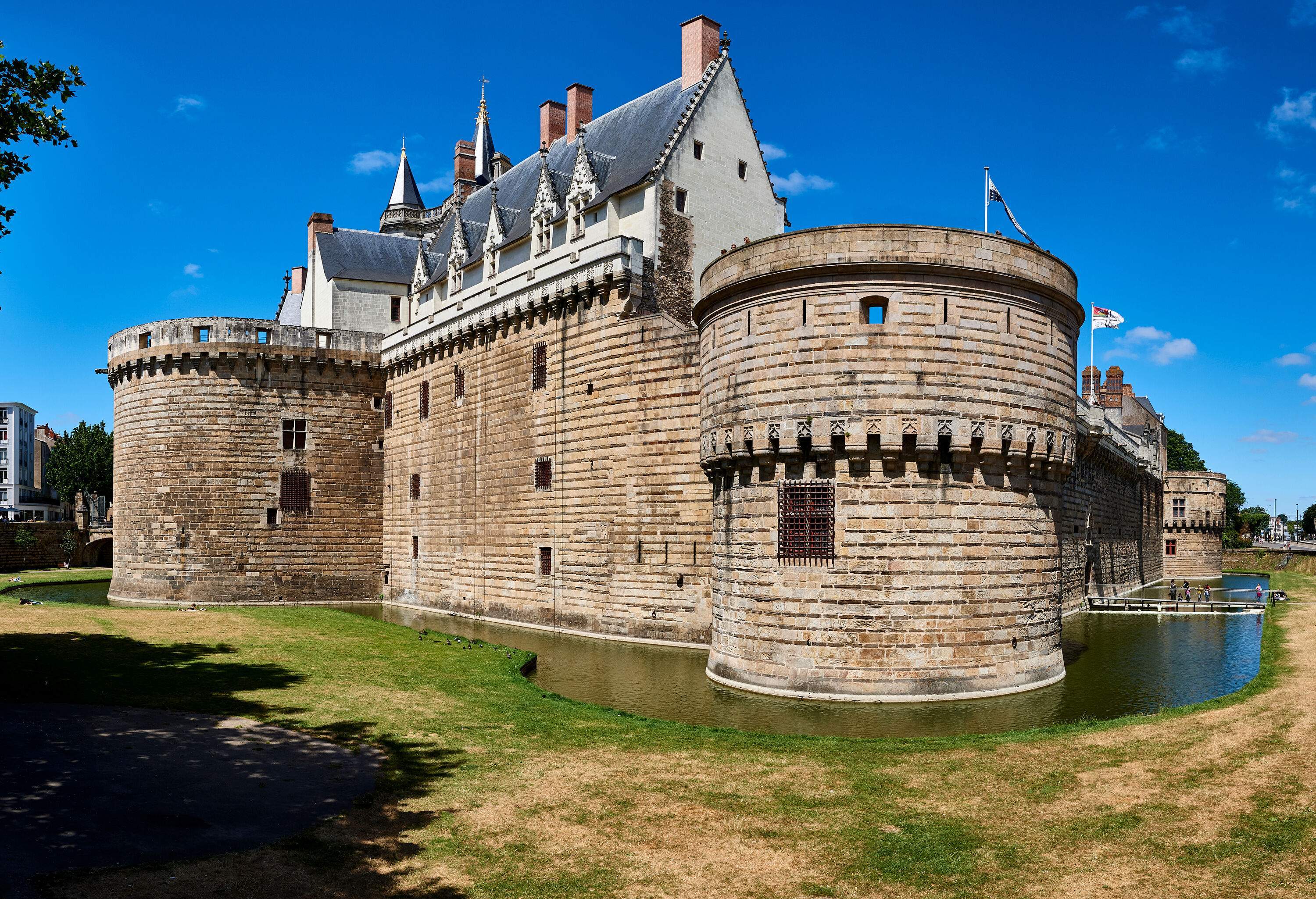 A historic castle with circular towers at each corner and a drawbridge for entrance, surrounded by a moat and grasslands.