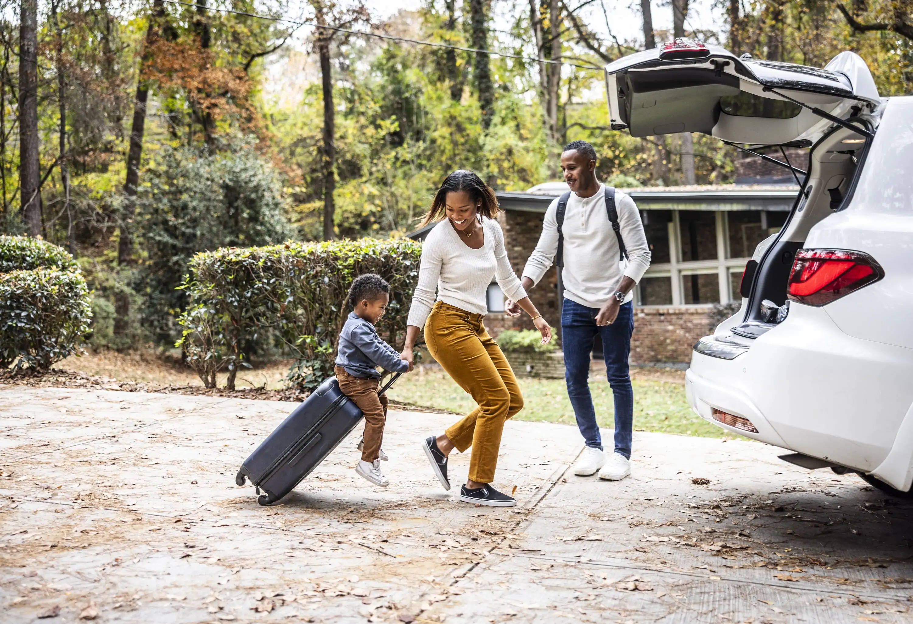 Mother pulling young boy on suitcase and loading car for family vacatio