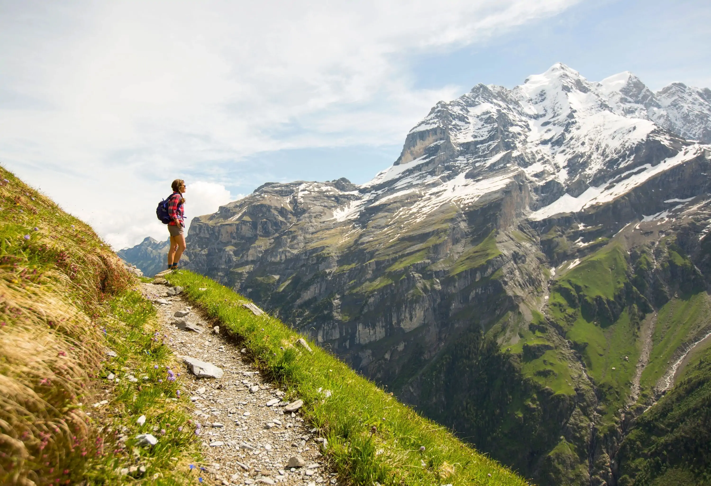female hiker on a path looking at snow capped mountain on a summer day