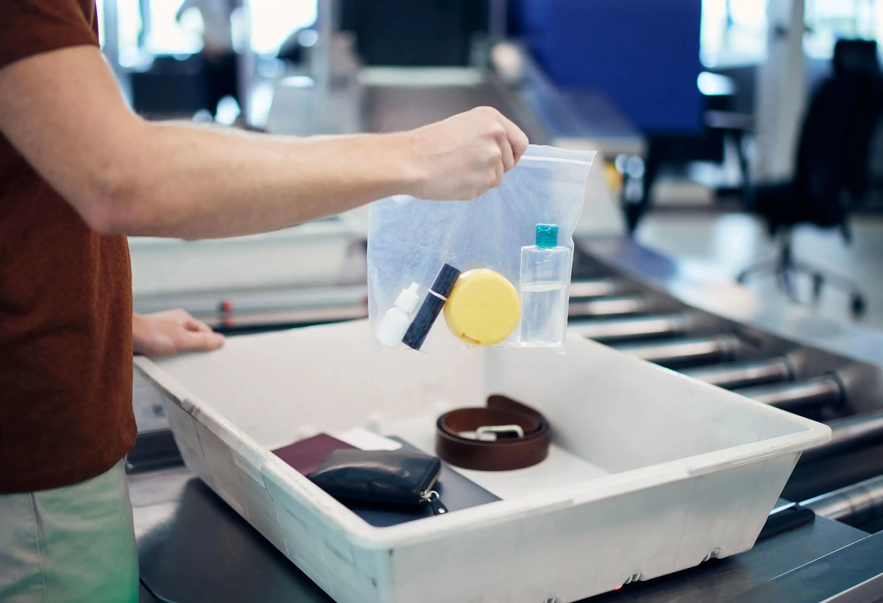 Airport security check before flight. Passenger holding plastic bag with liquids above container with laptop and personal items