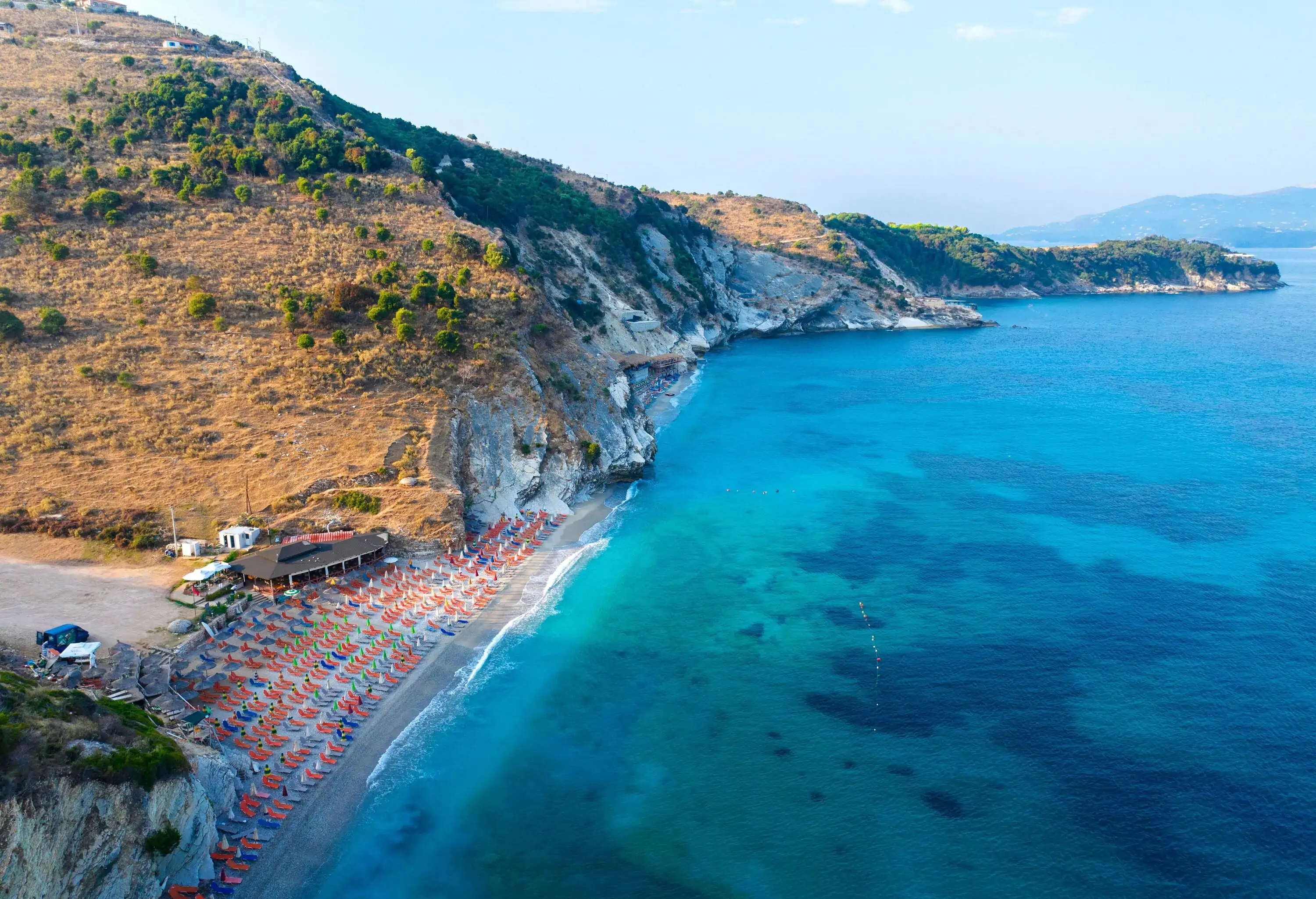Aerial view of a beach in a cove with orange sun umbrellas and crystal clear blue water