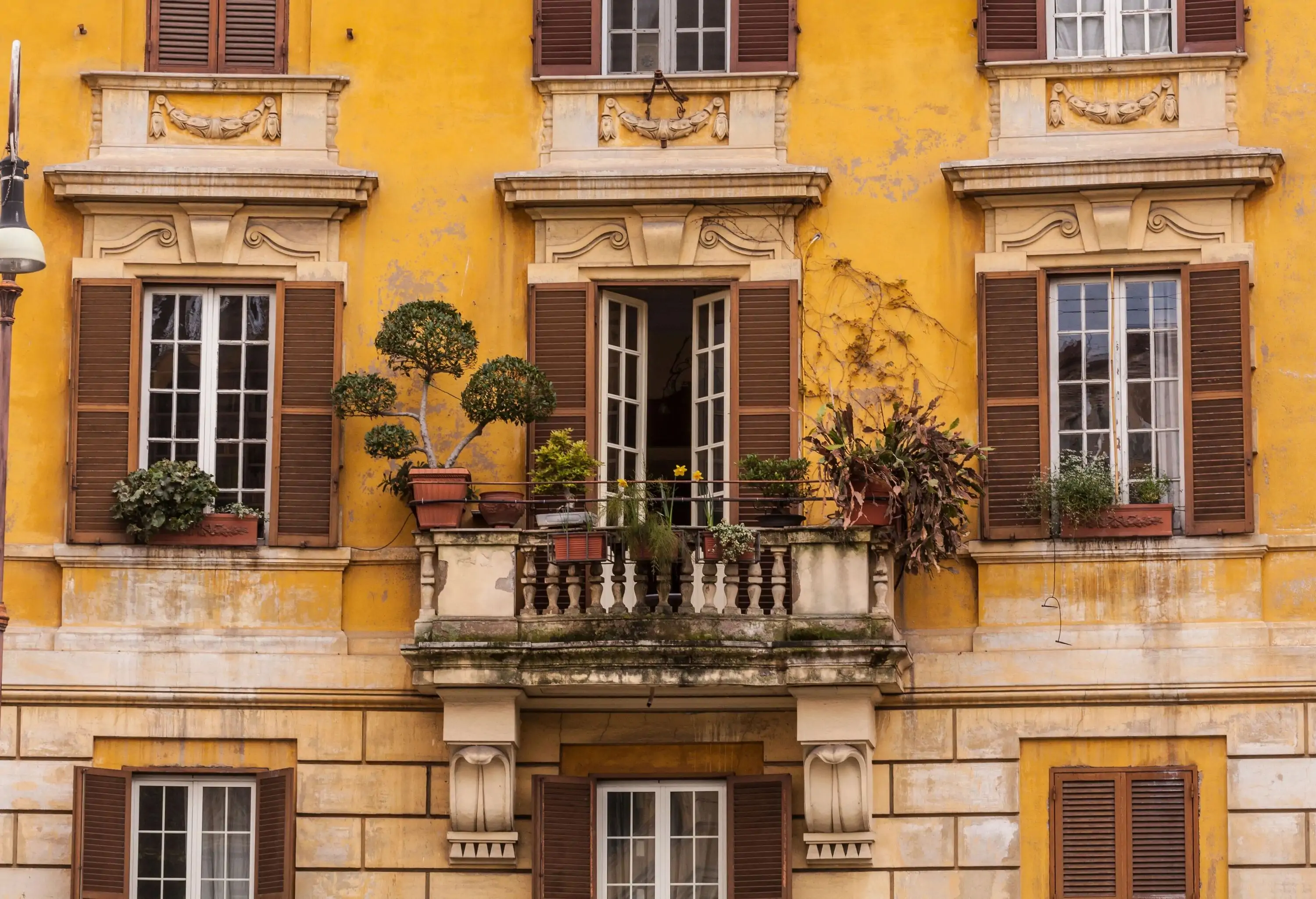 An old Italian building with yellow walls and wooden window shutters.