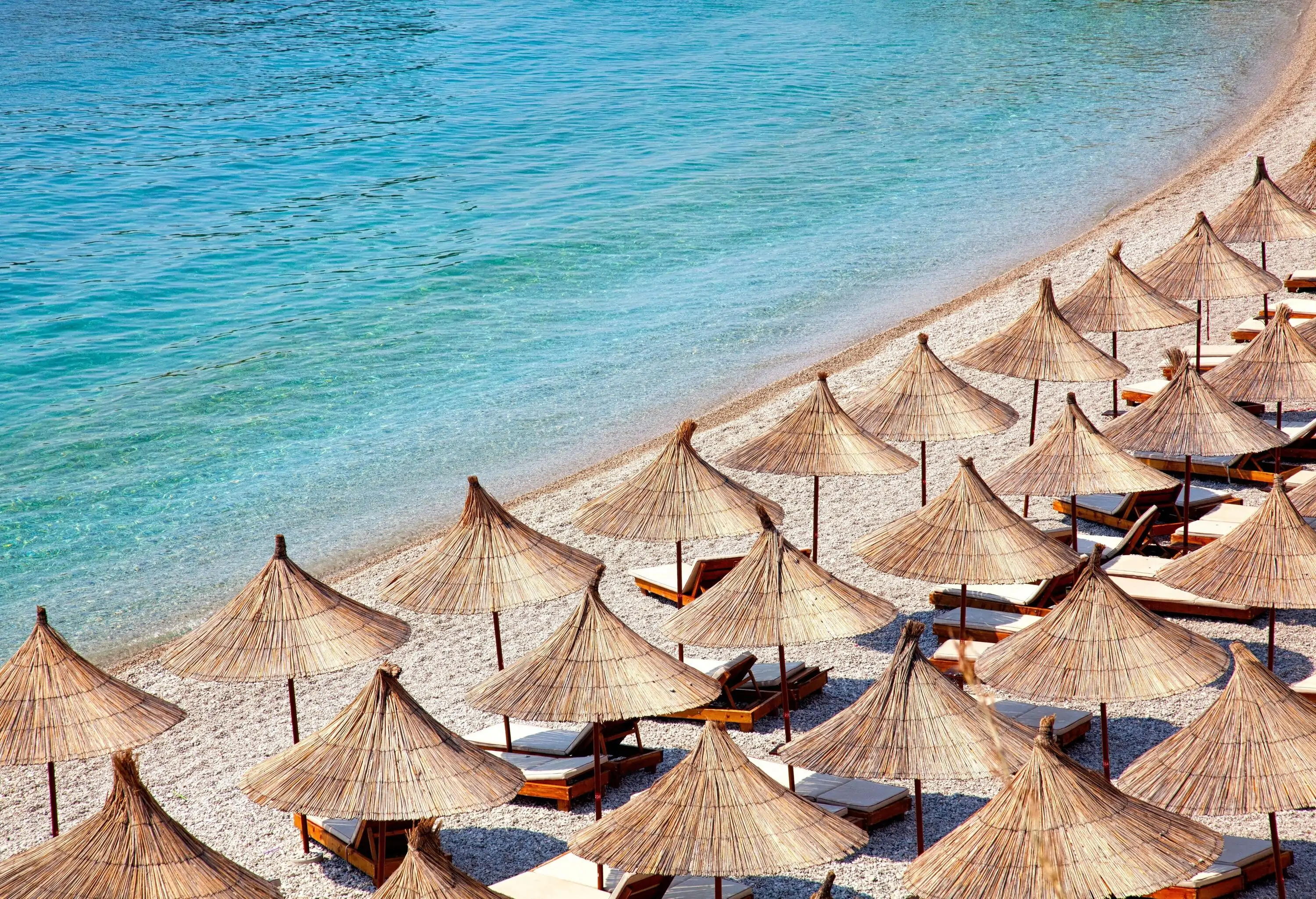 A beach with rows of sunbeds under thatched umbrellas.