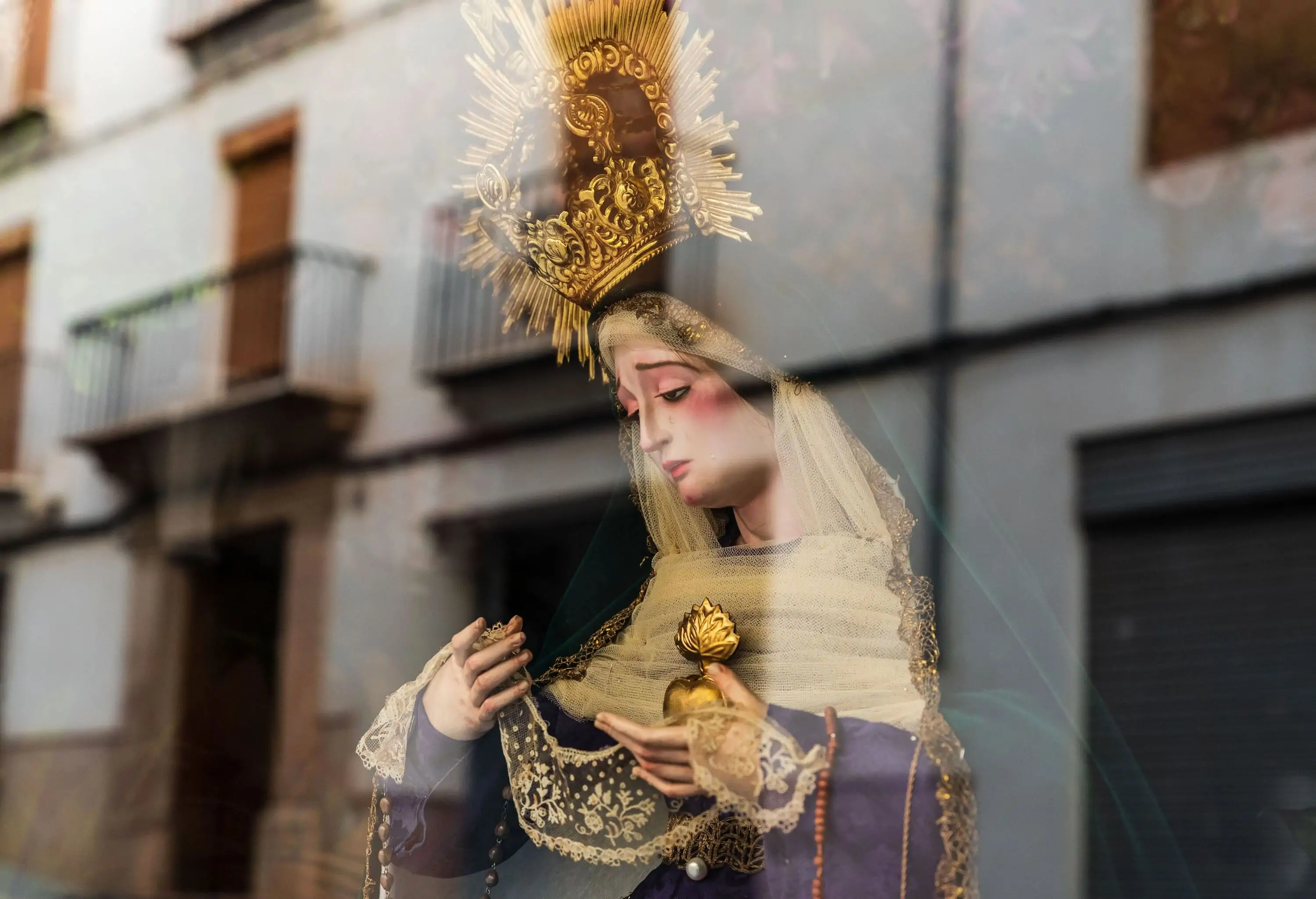 A glass window displaying a statue of a female religious figure dressed in a lavish cloak and a gold crown.