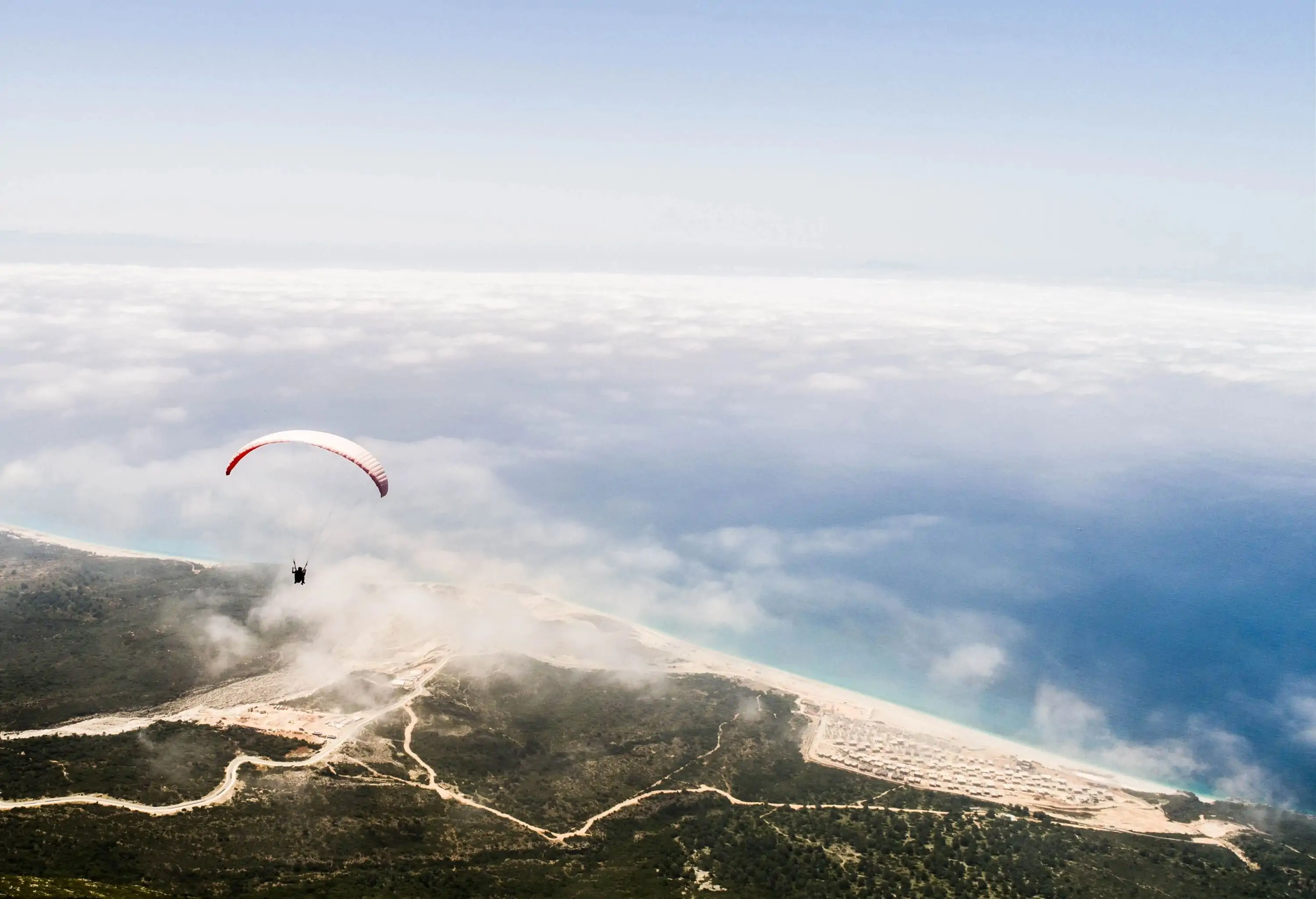 High angle view of a person paraglyding over a mountain range culminating on a beach