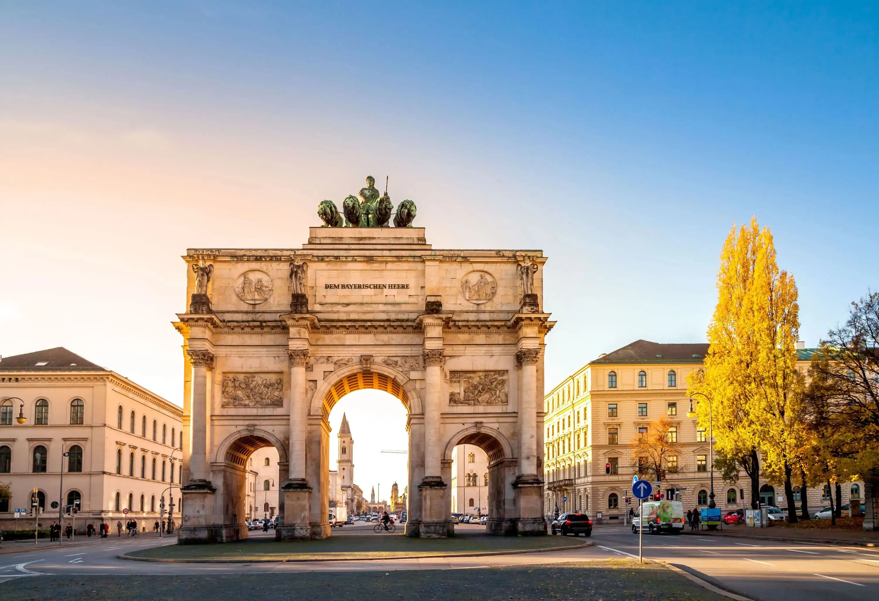 A massive three-arch monument atop a bronze statue with four lions overlooking the surrounding buildings on a roundabout.