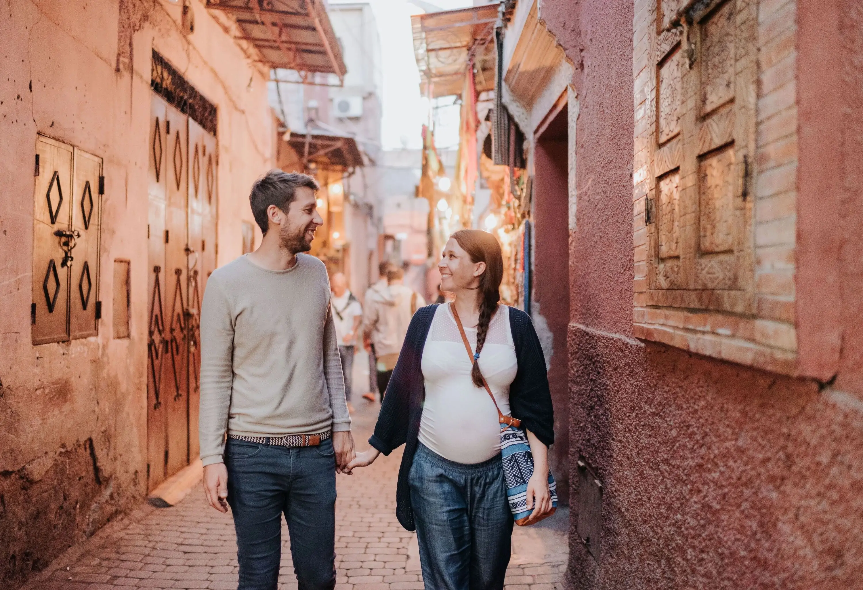 A man and his pregnant wife on a narrow street lined with traditional houses.