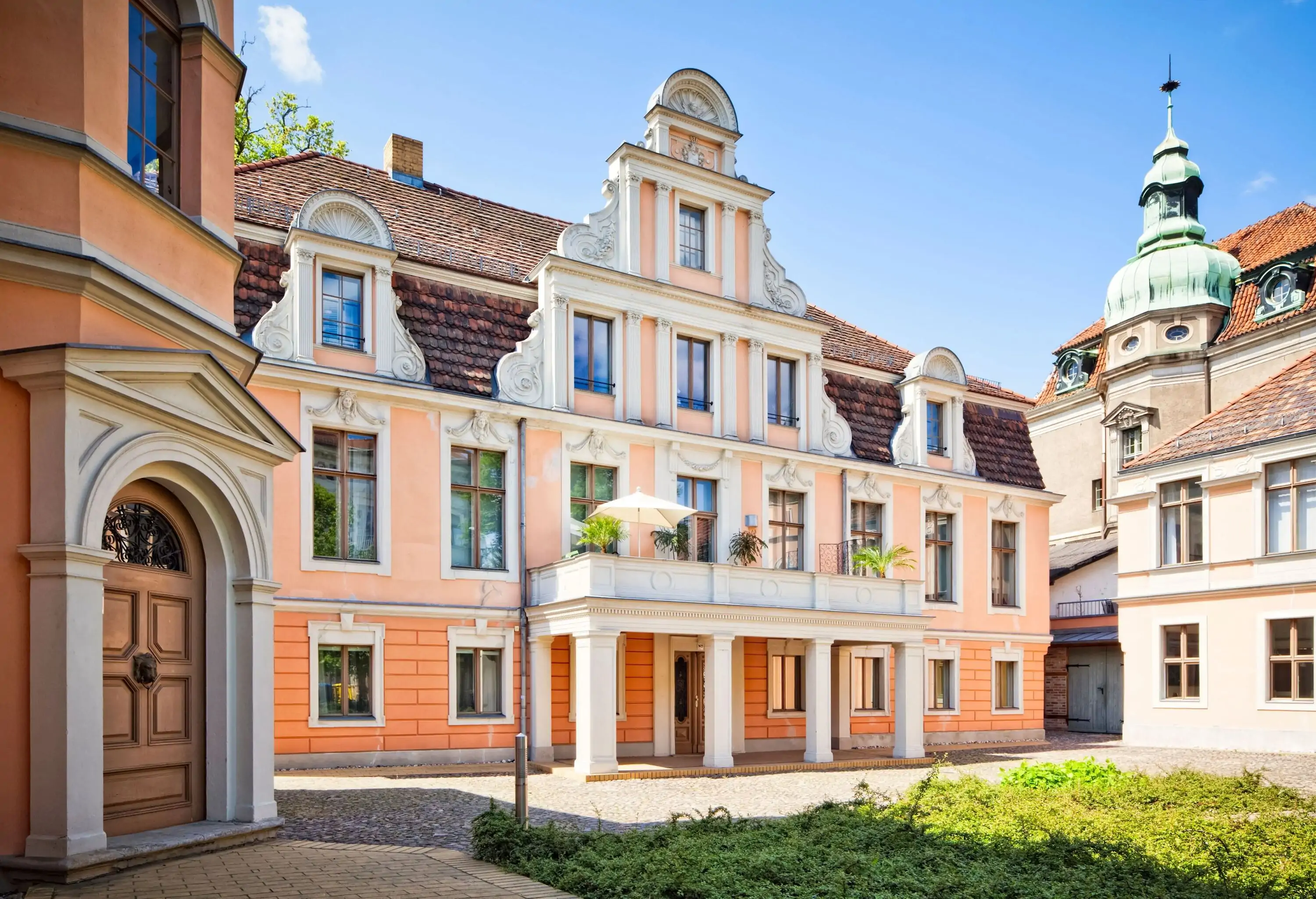 A manor house's façade with a Flemish gable roof and a balcony on top of its portico.
