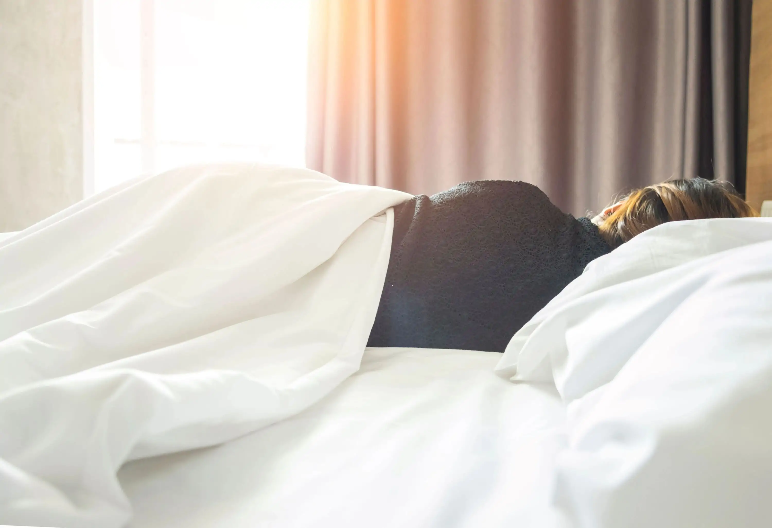 A woman sleeping on her side as the sunlight strikes through the glass window.