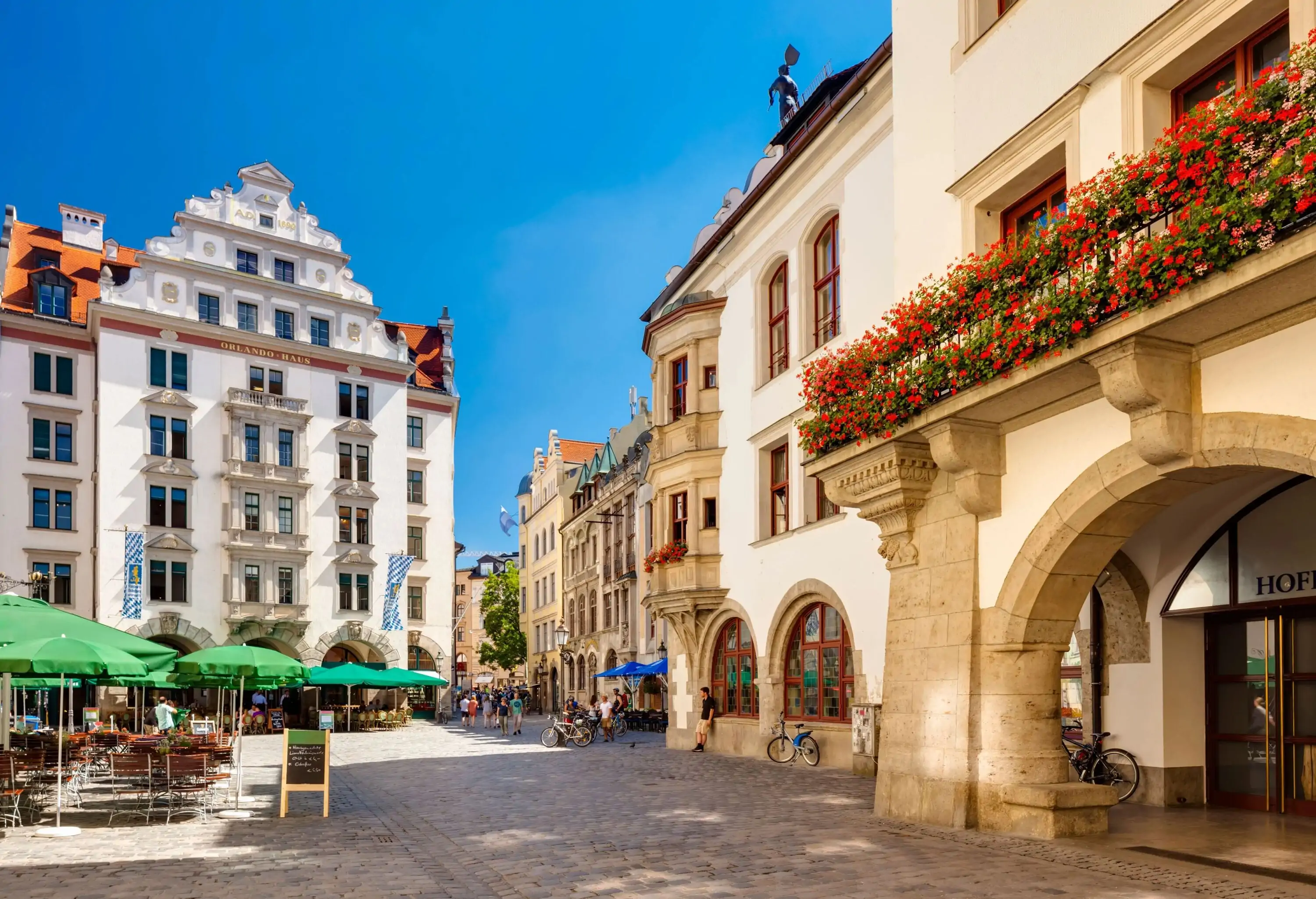 People stroll on a street with outdoor dining areas lined with adjacent buildings.
