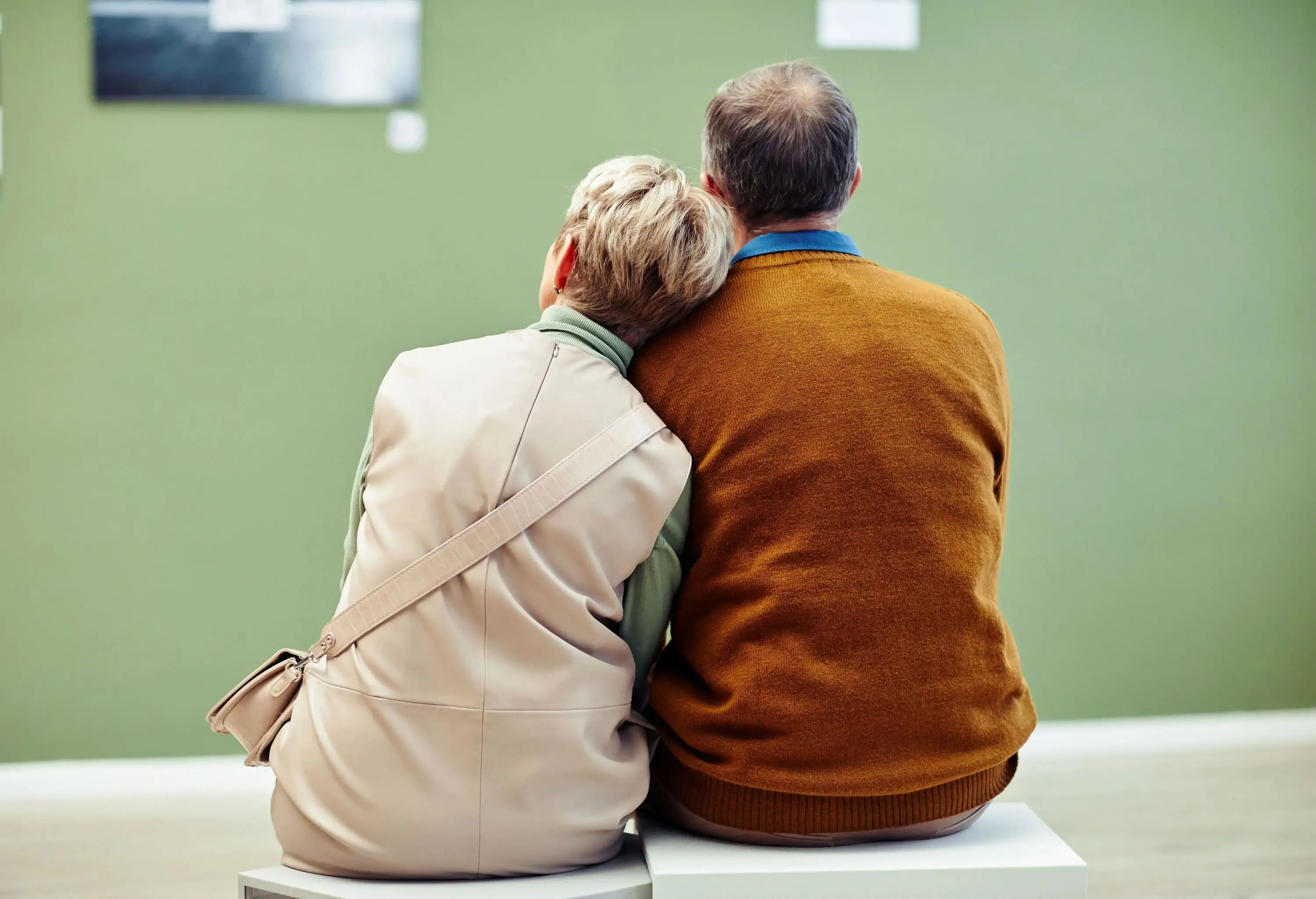 Rear view of a sweet elderly couple leaning on the man's shoulder while sitting inside the museum.