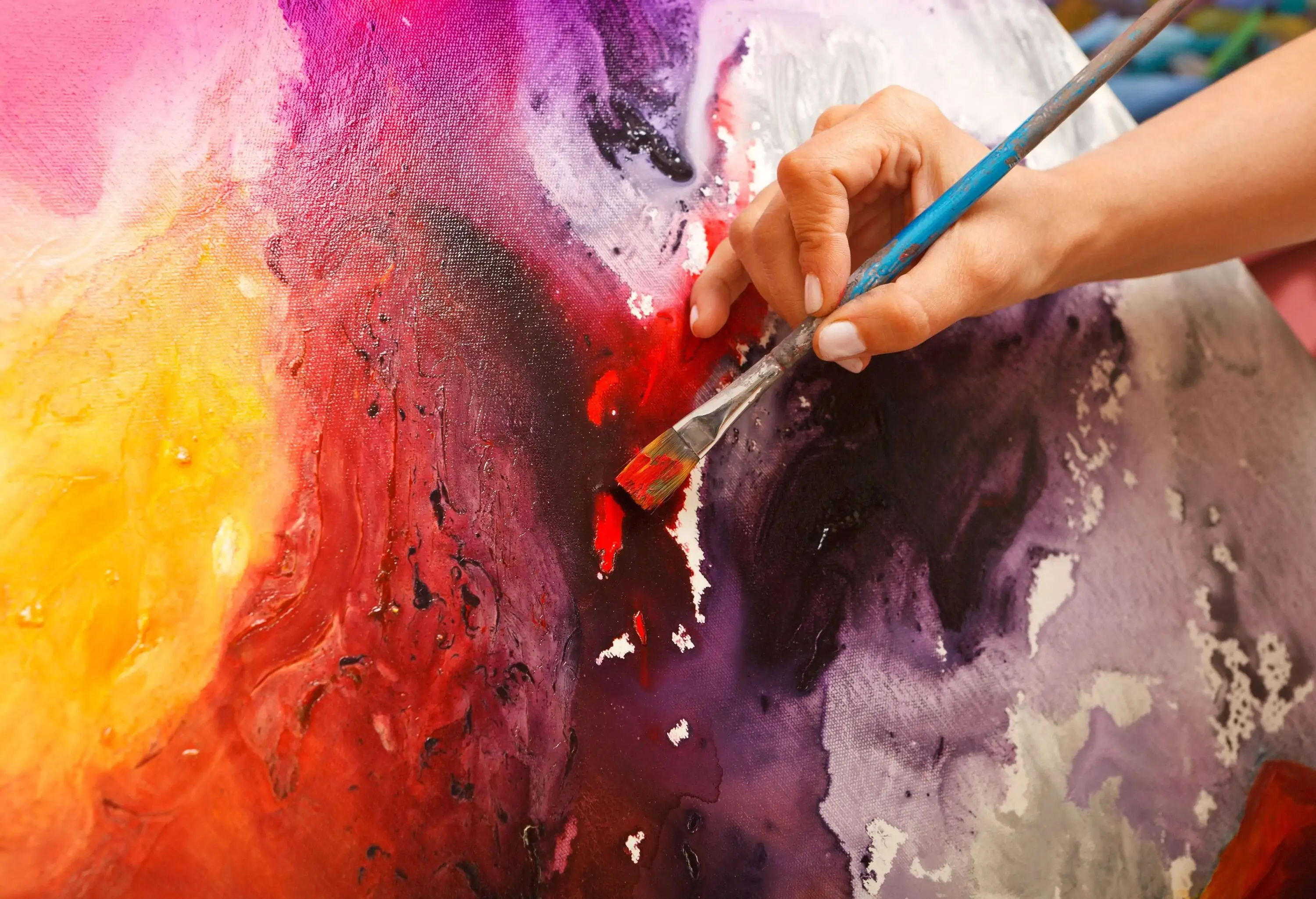 A painter brushing red paint on a canvas with splashes of other hues.
