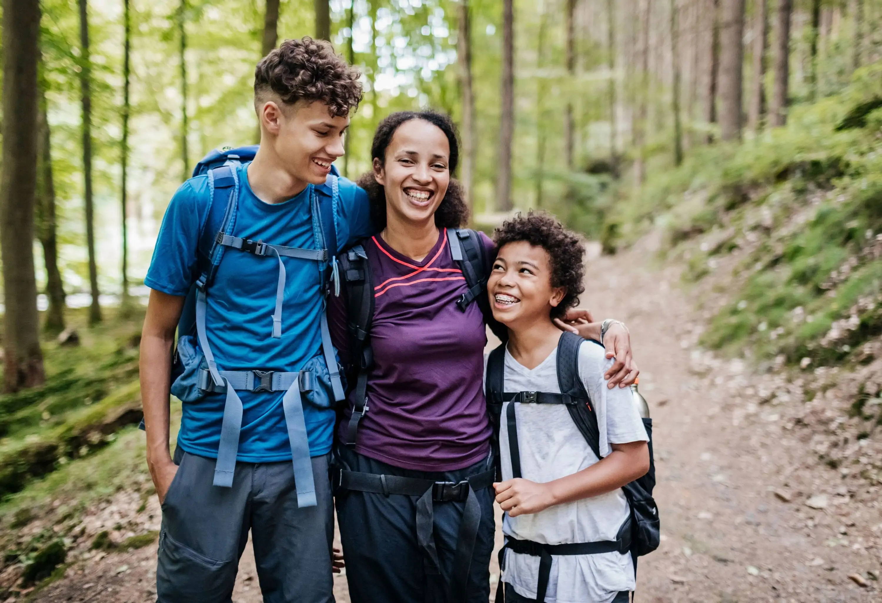 A woman sandwiched between two boys as they stroll through the woods.