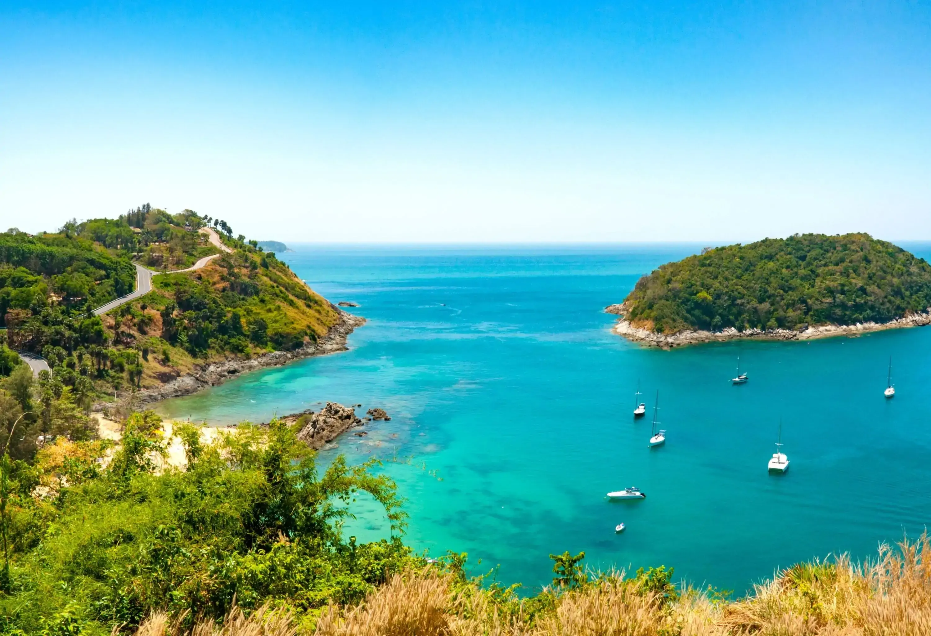 A panoramic tropical ocean landscape features boats anchored near a serene wooded island.