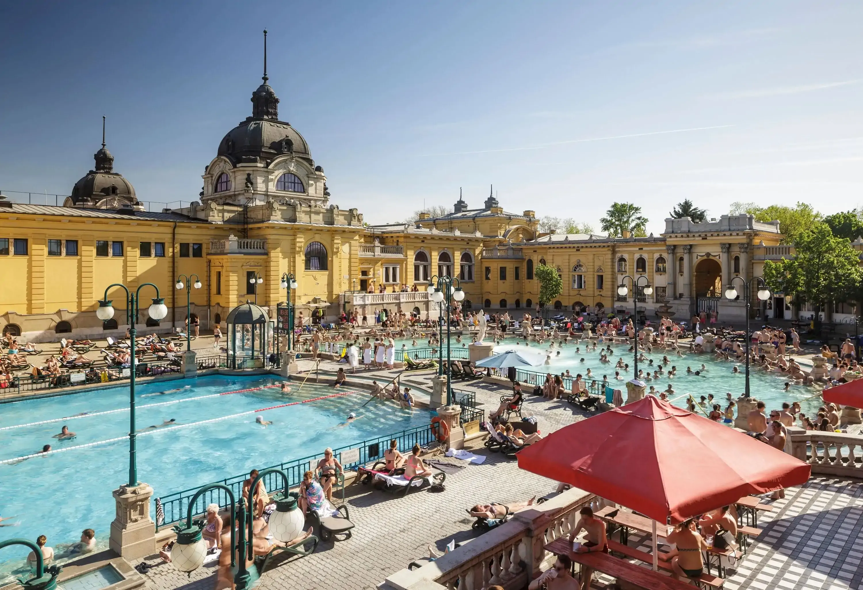A crowded swimming pool inside an ancient Neo-Baroque-style thermal bath.