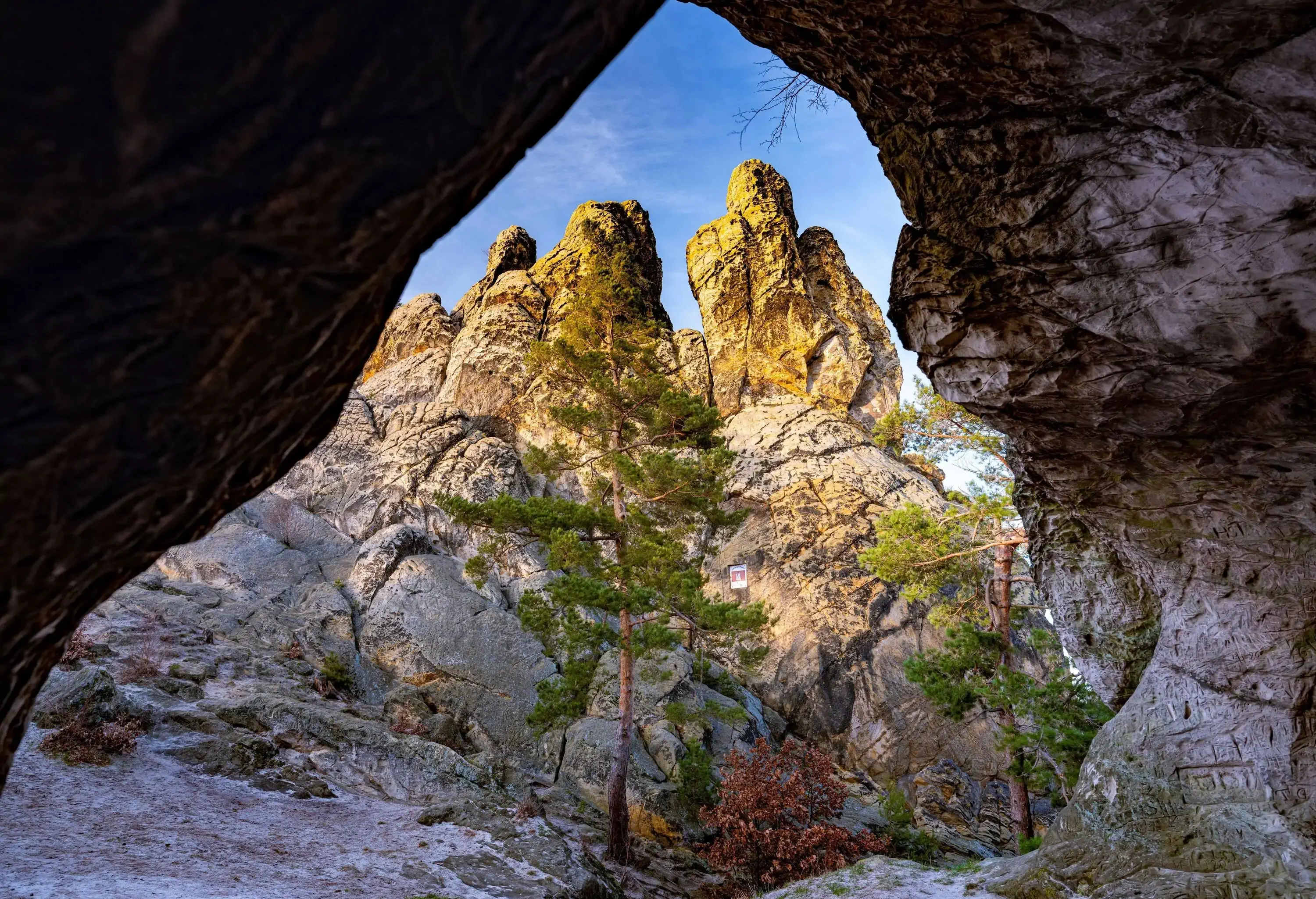 A rocky mountain formation with few trees beneath is seen from a keyhole of a cave.