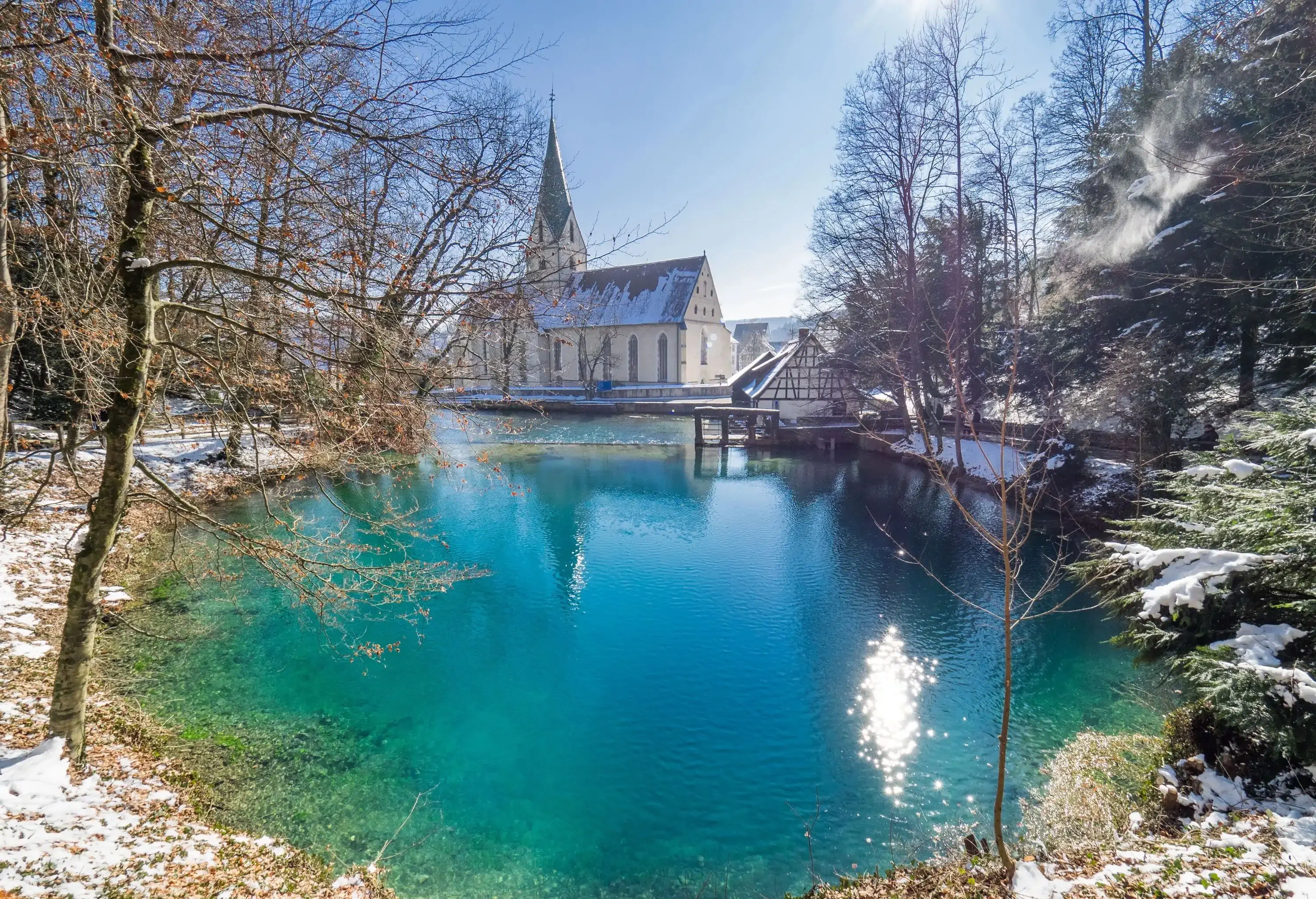 A turquoise lake surrounded by bare trees and a nearby monastery.