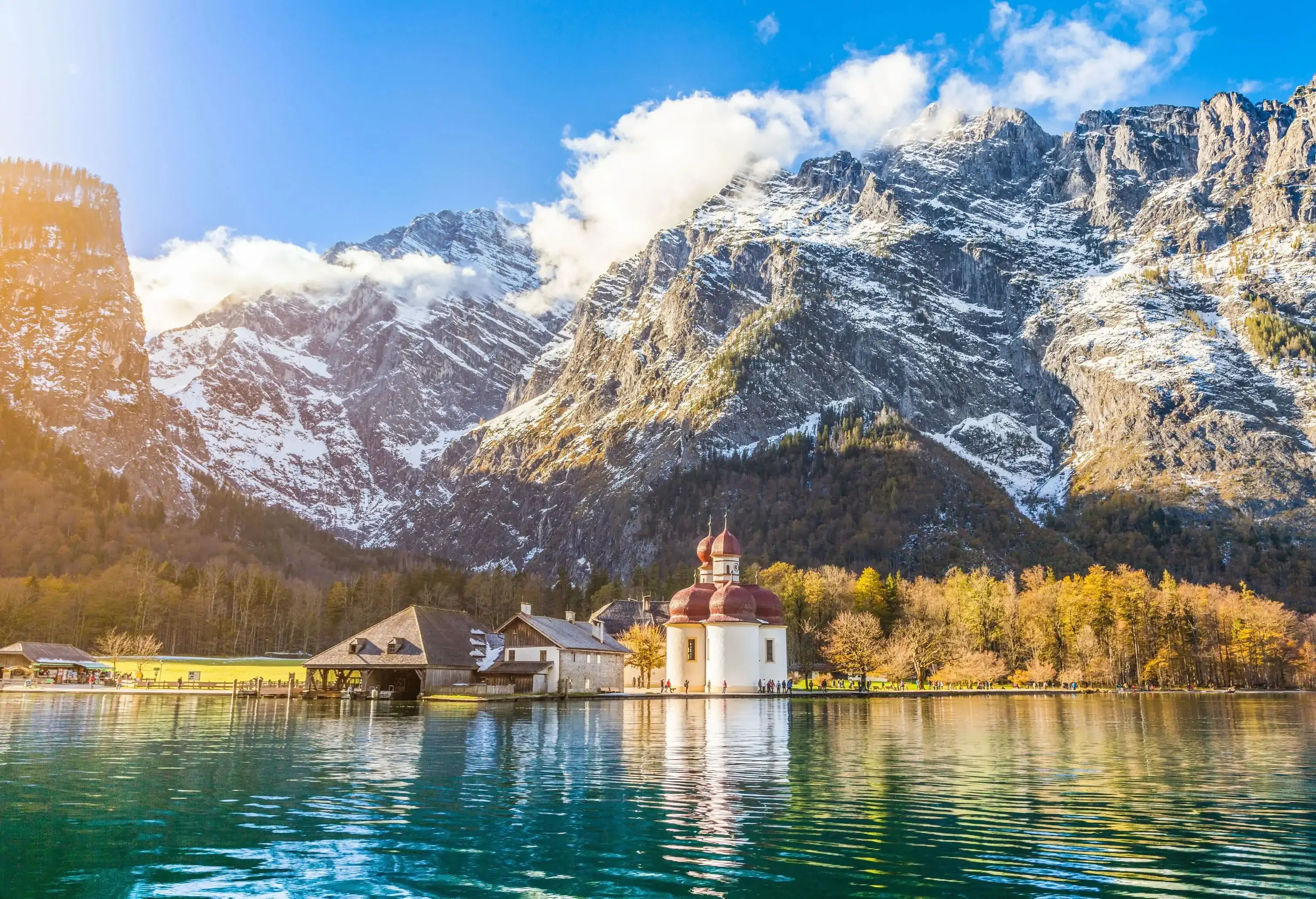 A lakeside domed church and old houses at the foothills of massive snow-covered mountains.