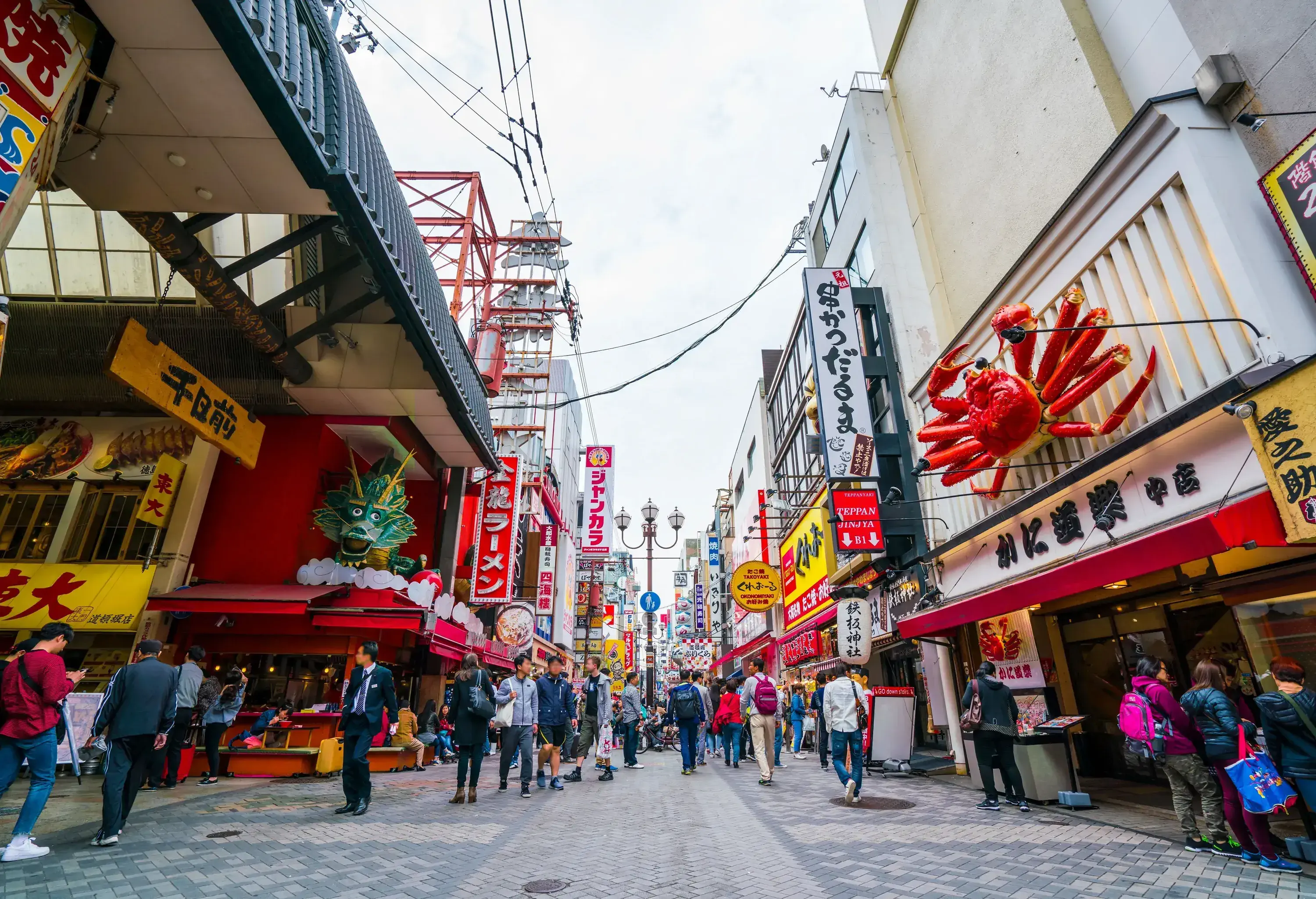 A crowded street lined with restaurants and shops with colourful advertisement billboards.