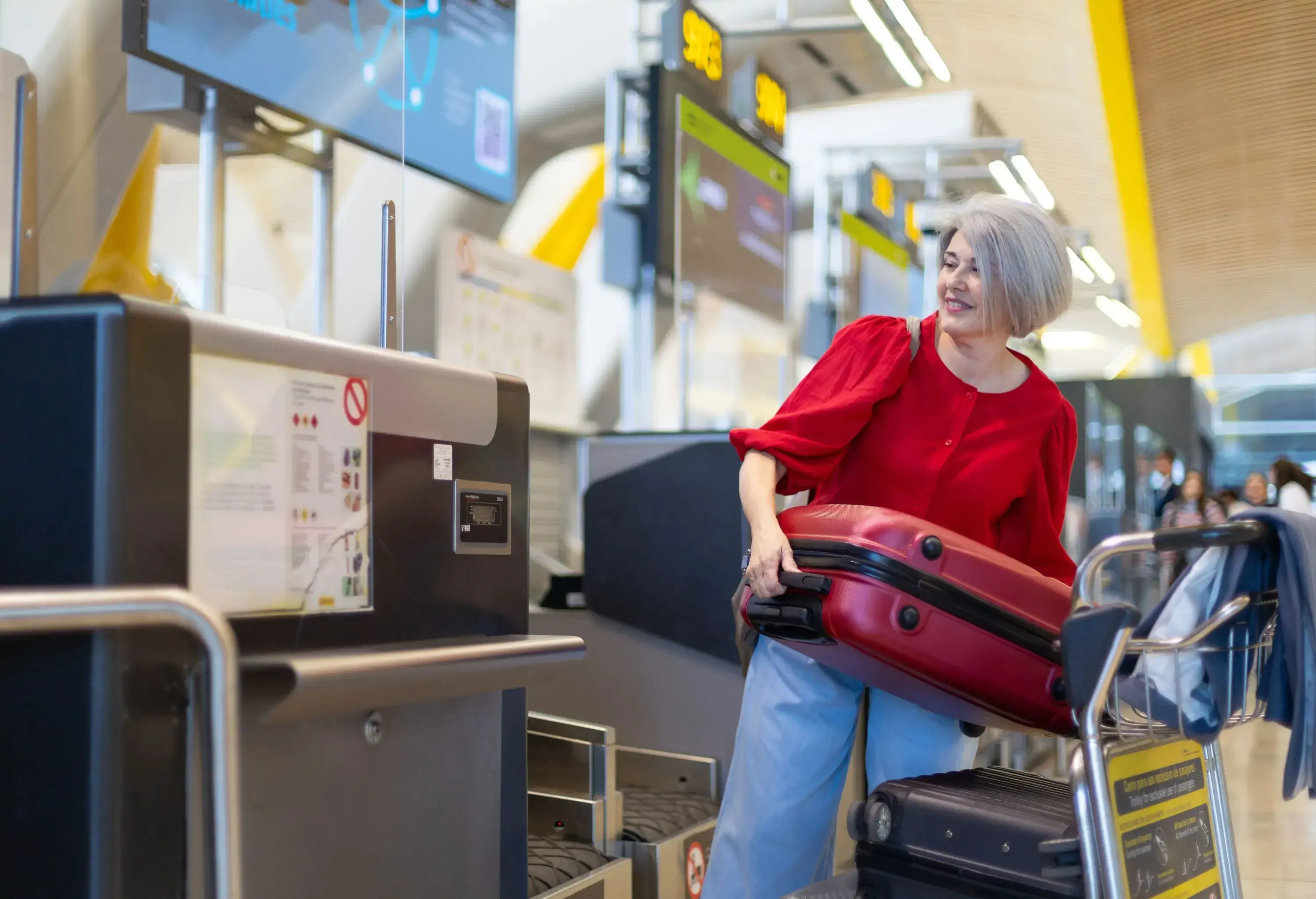 Mature tourist dropping her suitcase on the conveyor belt at the airport check-in area, ready for her flight