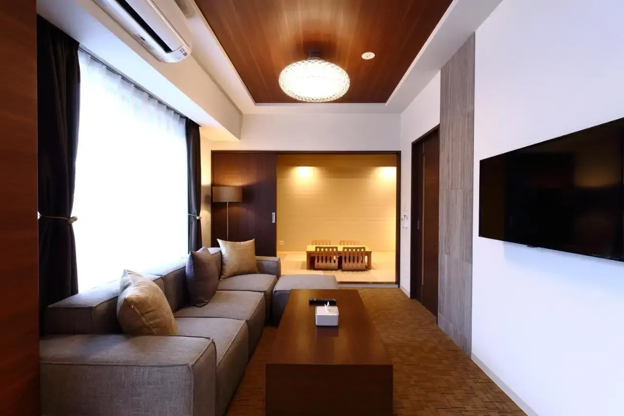Hotel lounge with grey sofa in front of tv with door over a dining room