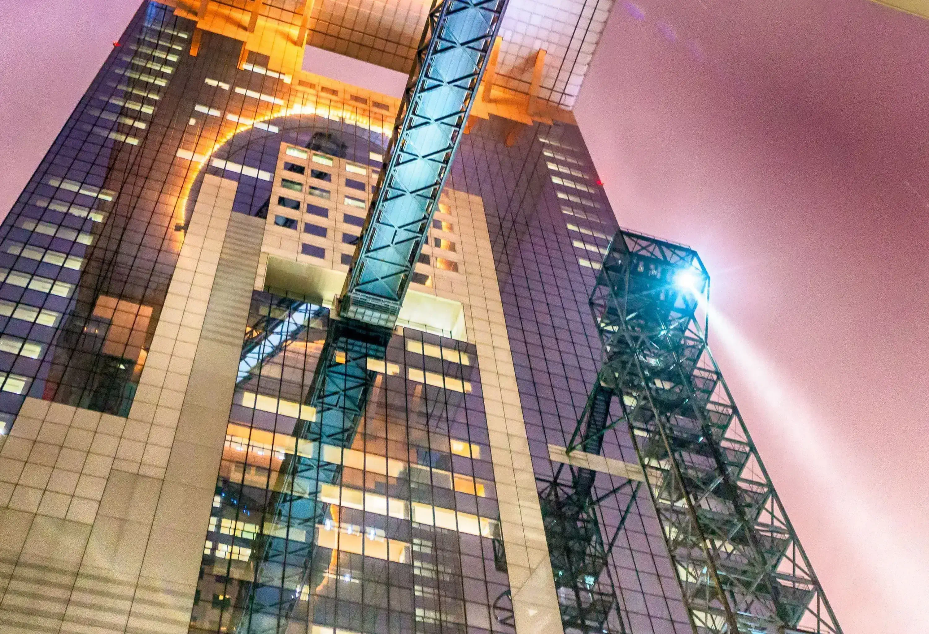A towering modern building with a glass facade is seen from street level at night.