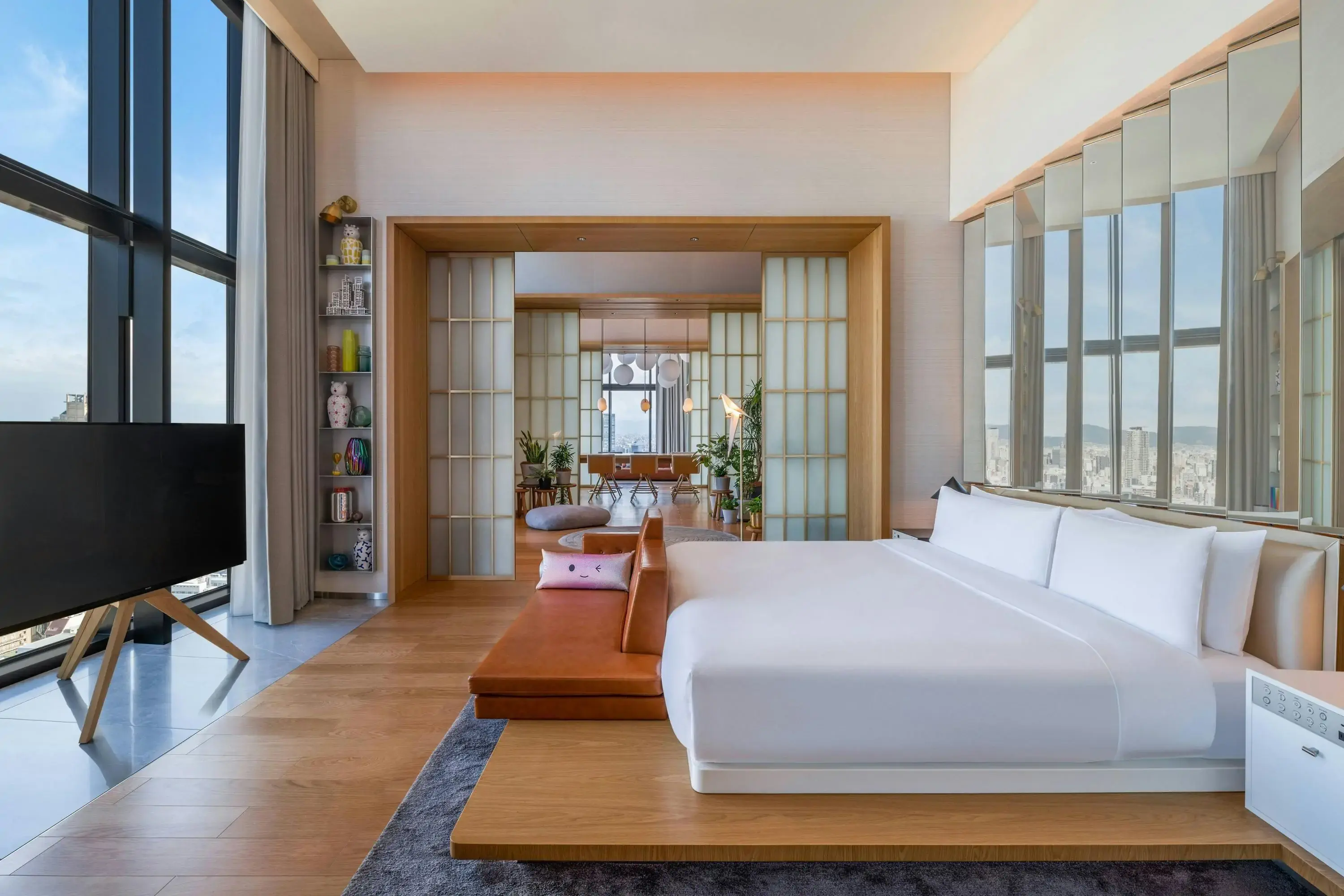 Luxury modern hotel room with bed overlooking large windows with city view and double doors to conference room