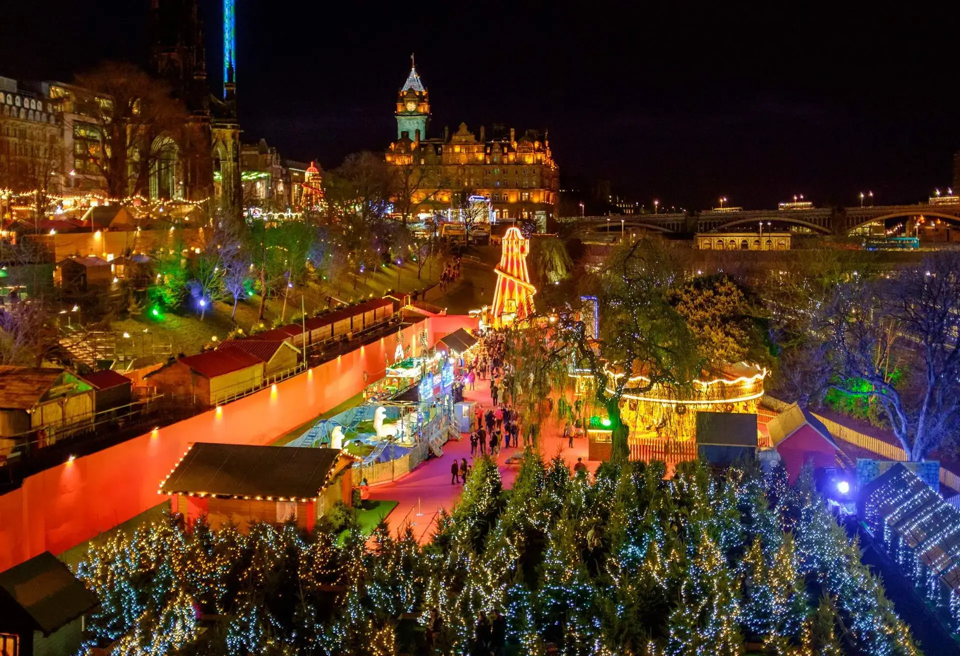 A lively Christmas market with a carousel, shops, and trees covered in lights.