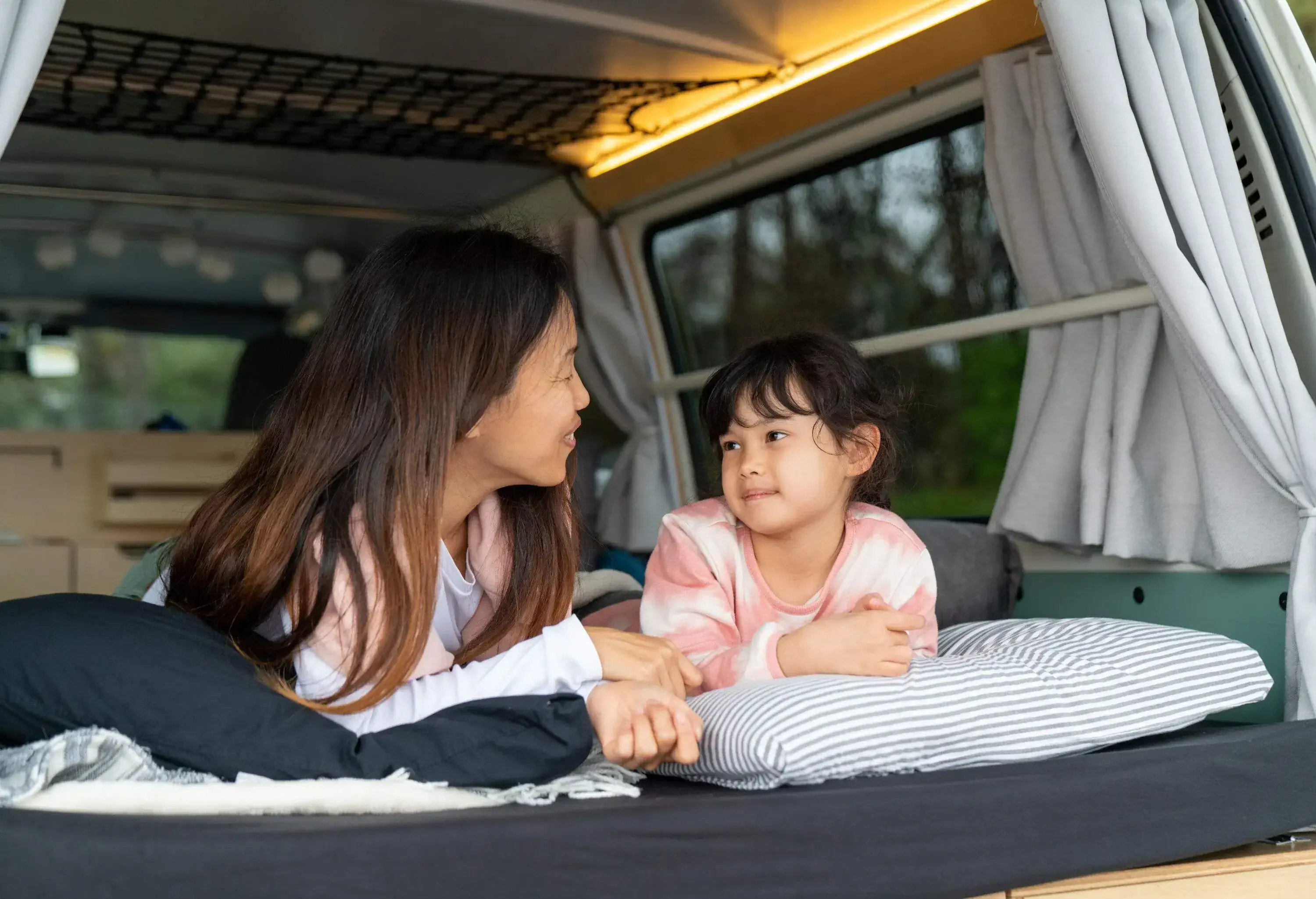A mother and child laying in bed at the back of an RV looking at each other.