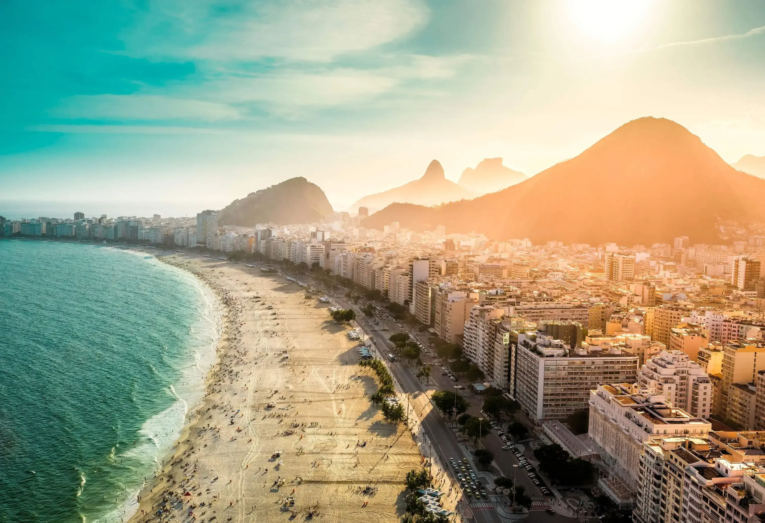 Massive buildings and mCopacabana Beach, a world-famous destination, bustles with sun-kissed beachgoers while the city's buildings elegantly line the coastline and towering mountains gradually fade into the distance.ountains on the coast overlooking the beach and the sea.