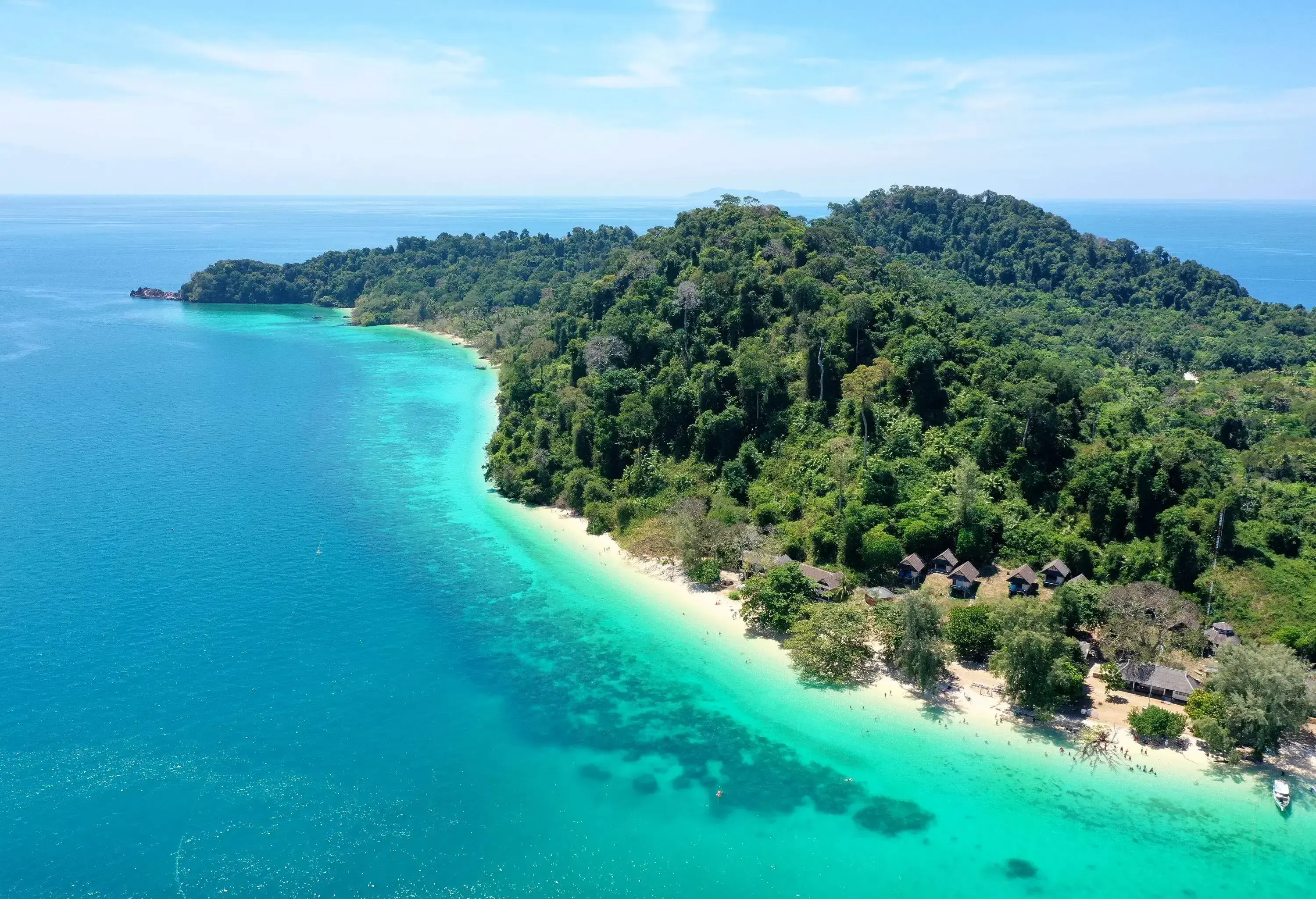 Aerial view of a forested island surrounded by the tranquil turquoise sea against the cloudy blue sky.