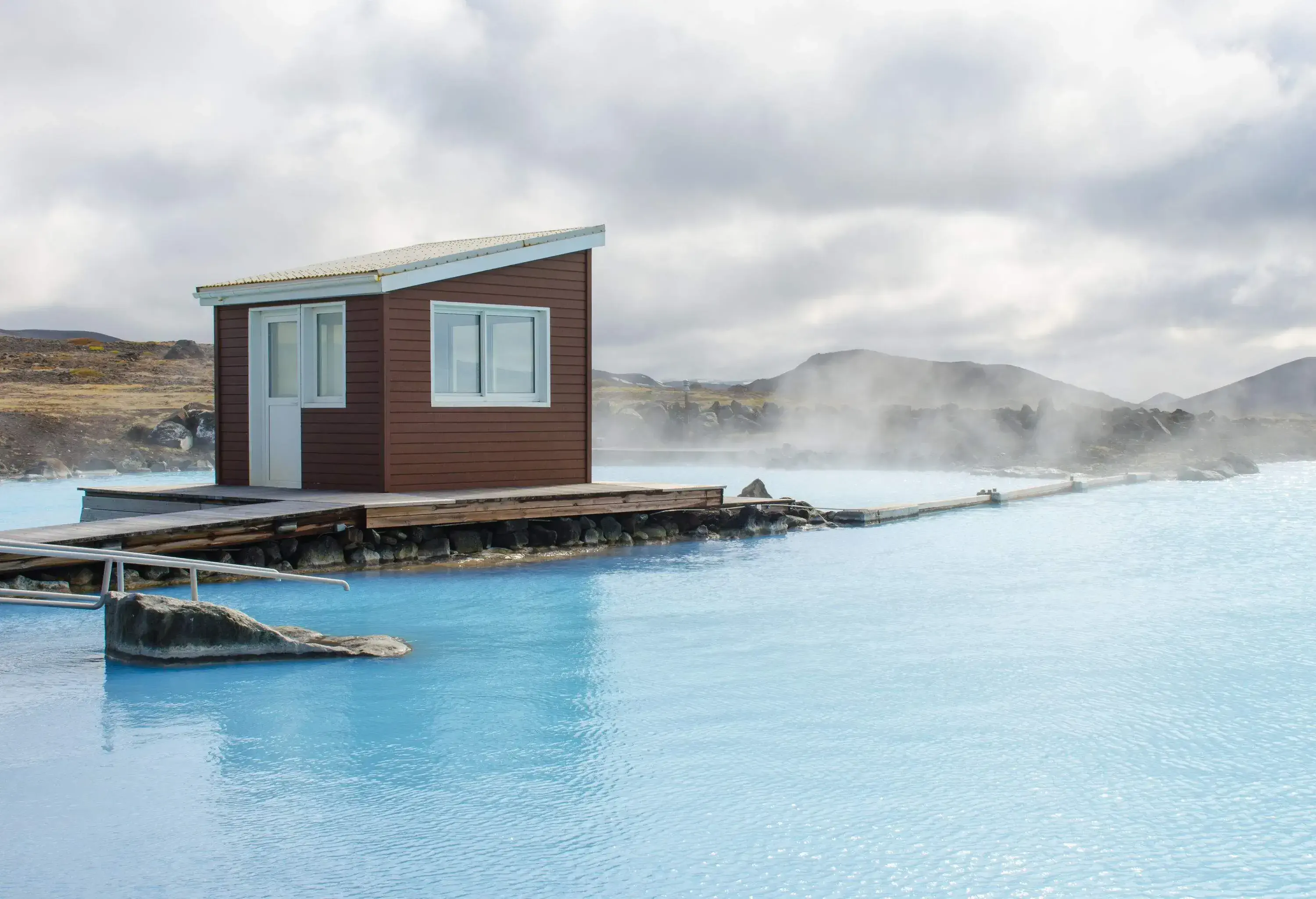 A brown cabin at the centre of a lake's steaming pool.