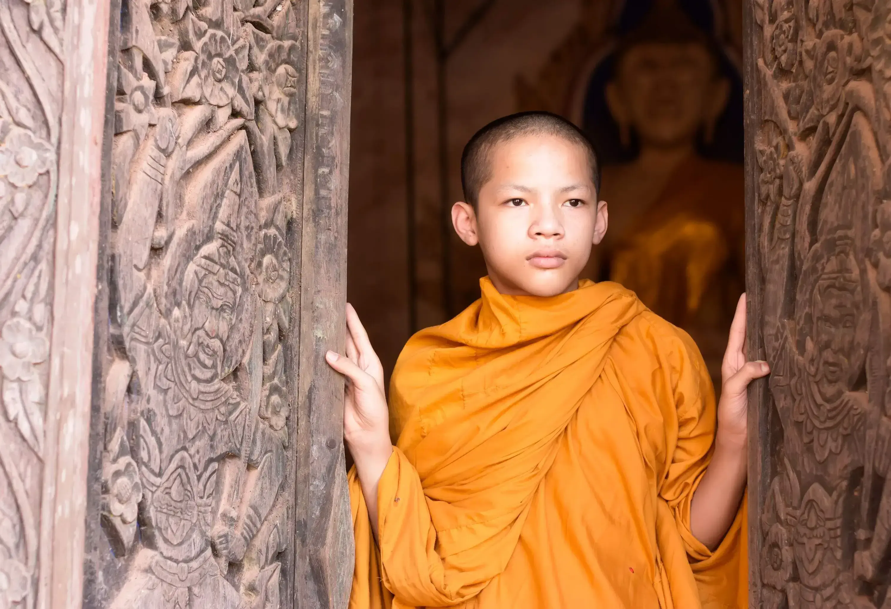 A young monk in traditional dress stands at the door of a temple.