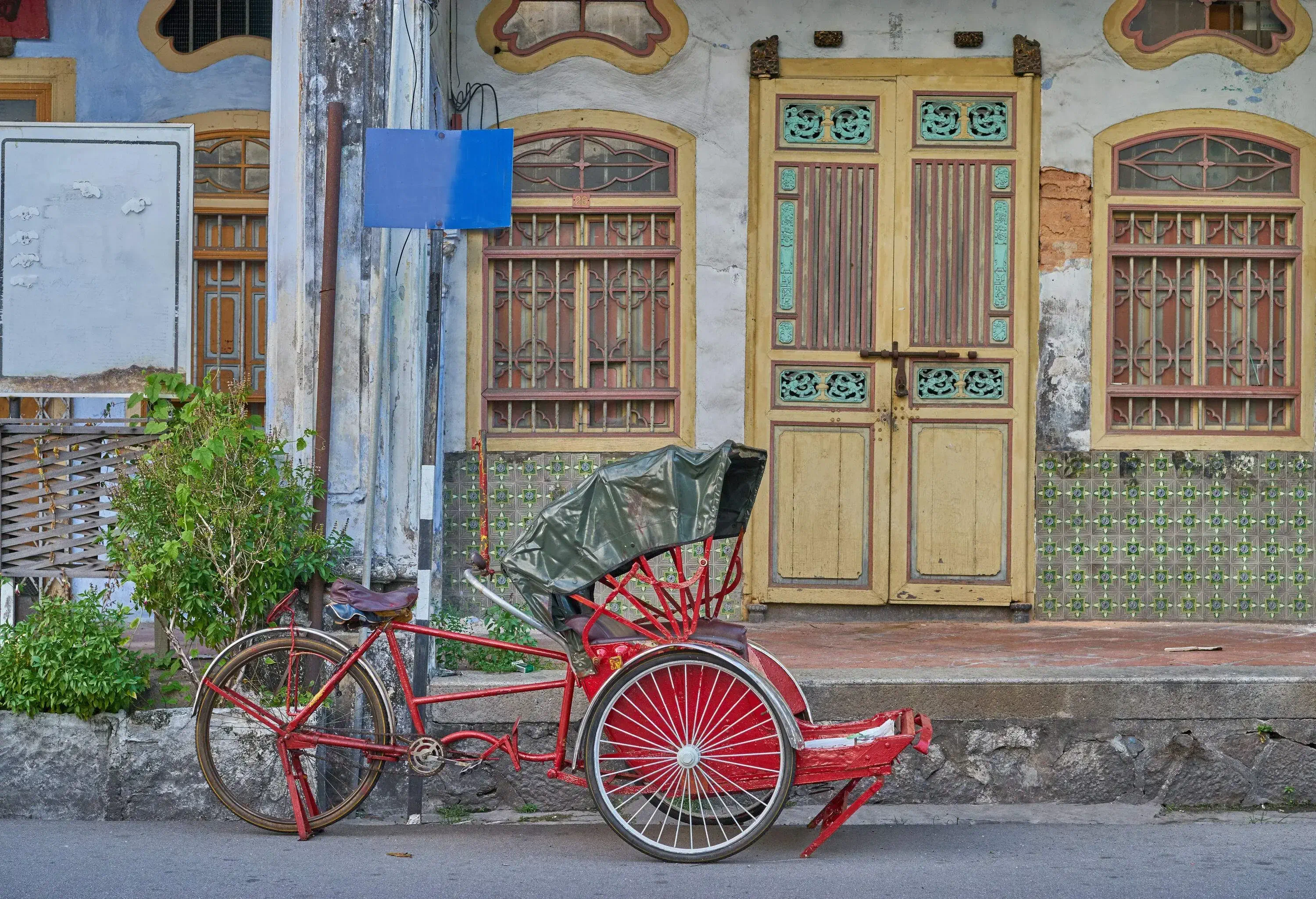 A classic red trishaw rests on the side of a street, flanked by charming old houses.