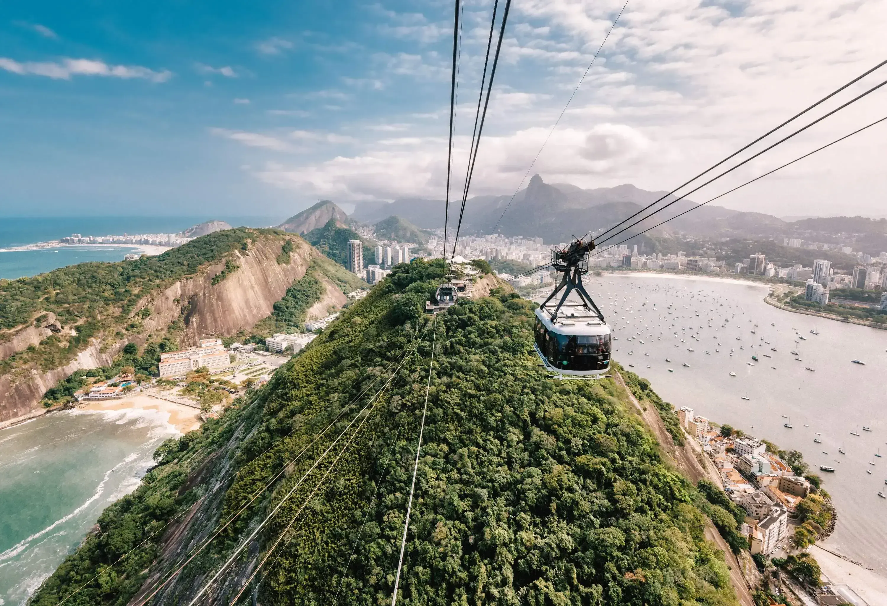 Ropeways running over a rock formation across the sea, which is littered with boats.