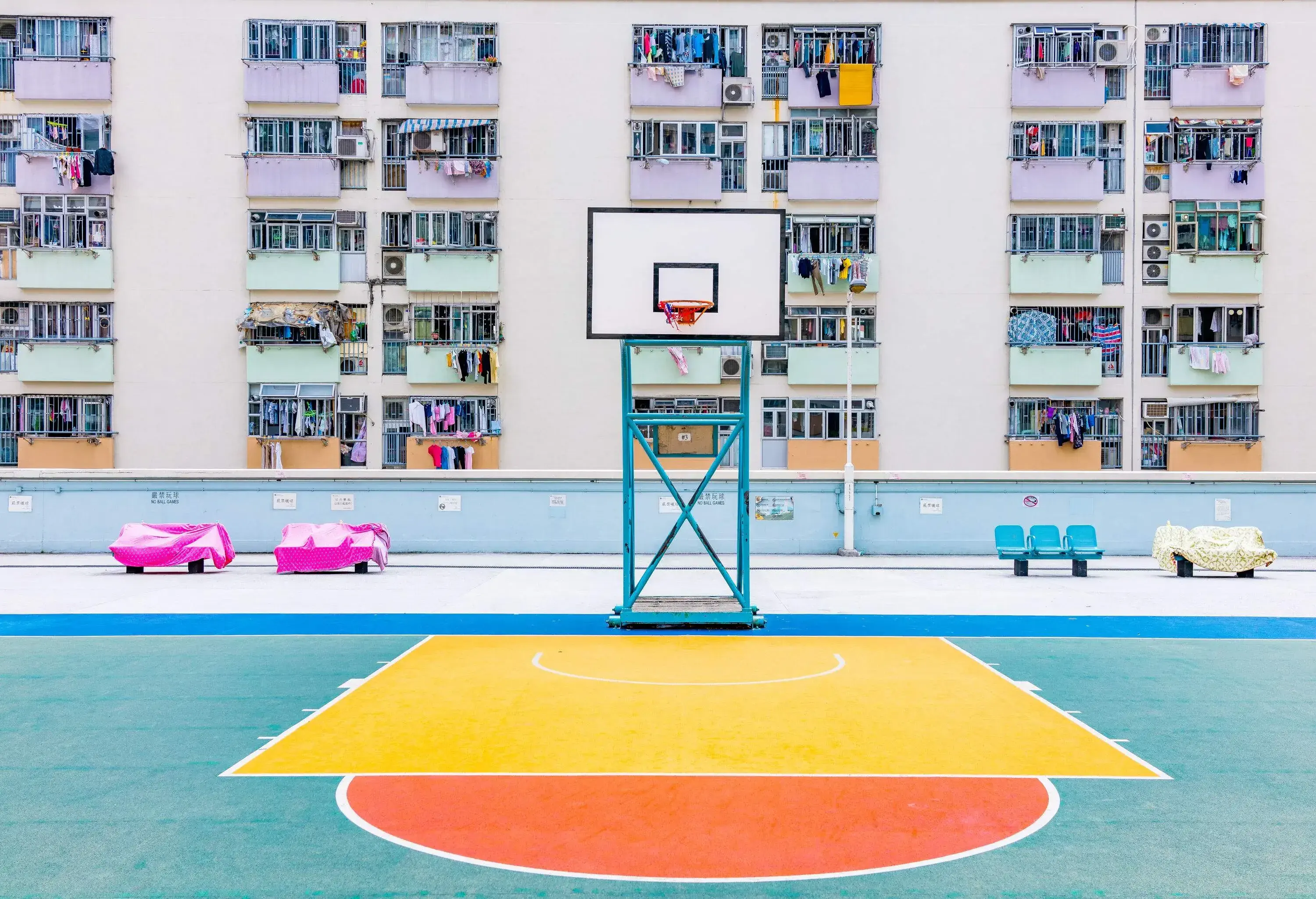 A colourful basketball court lined with benches along the walls of an apartment building.