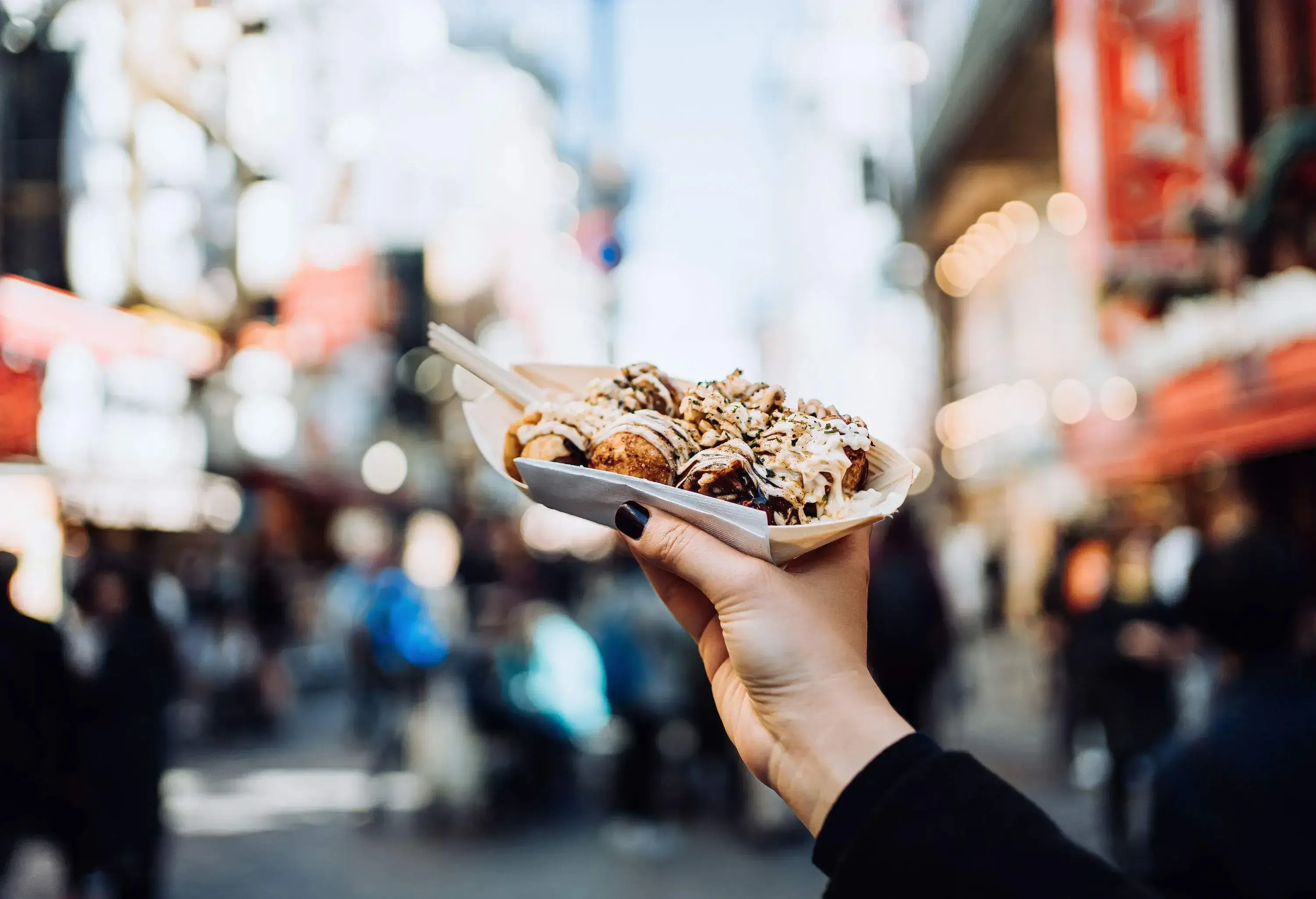 A female traveller's hand delicately handles a serving of freshly cooked traditional Japanese street-style snack takoyaki.