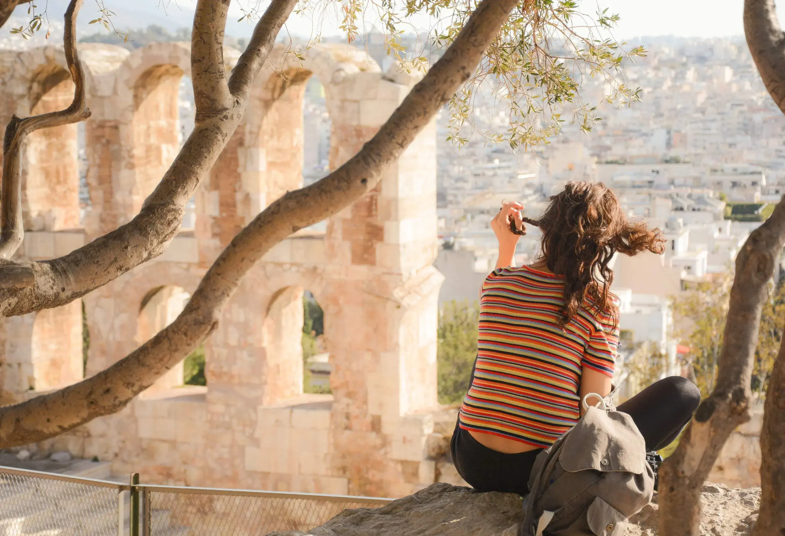 A woman sitting on top of a wall with boughs hanging behind her.