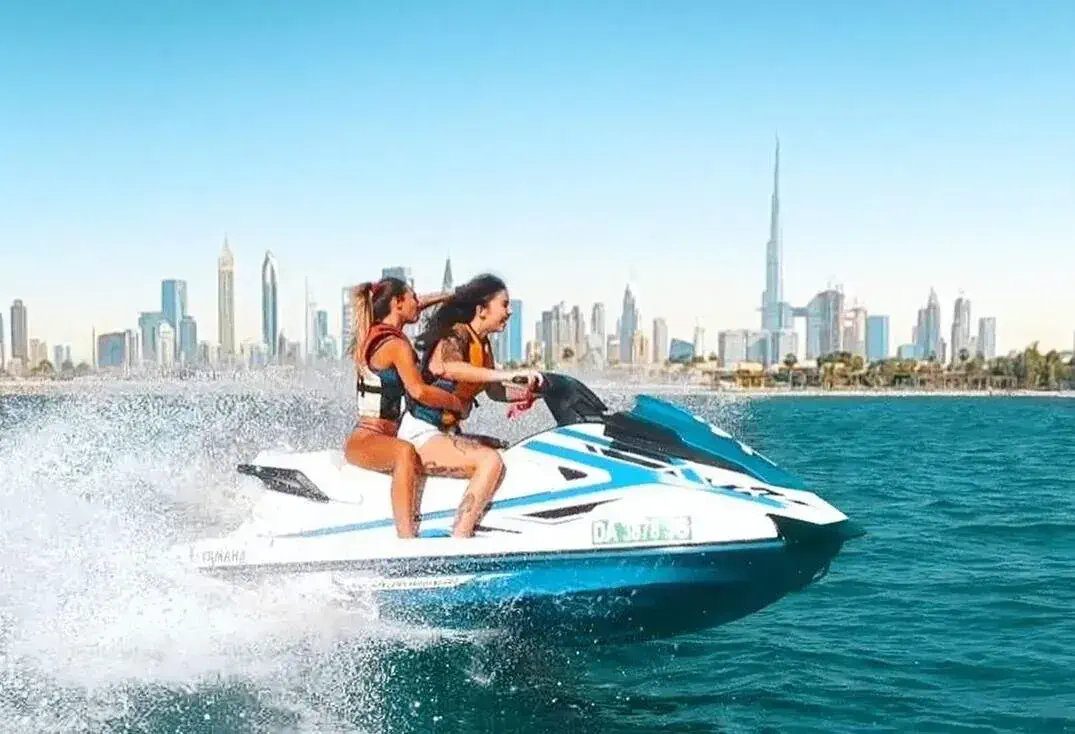 Two women riding jetski in the sea with modern cityscape in the background