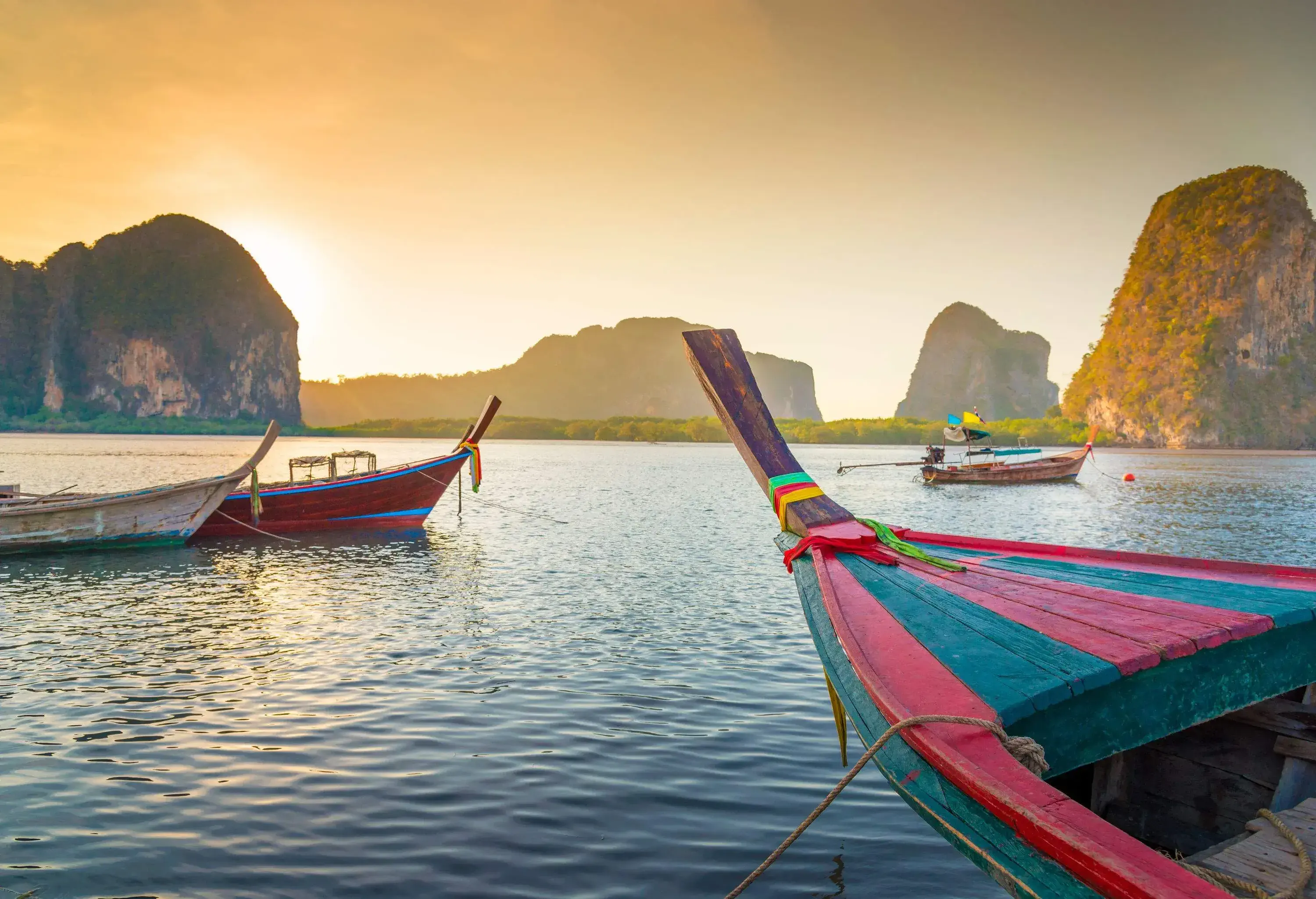 Colourful wooden boats anchored in the sea studded with rock cliffs.